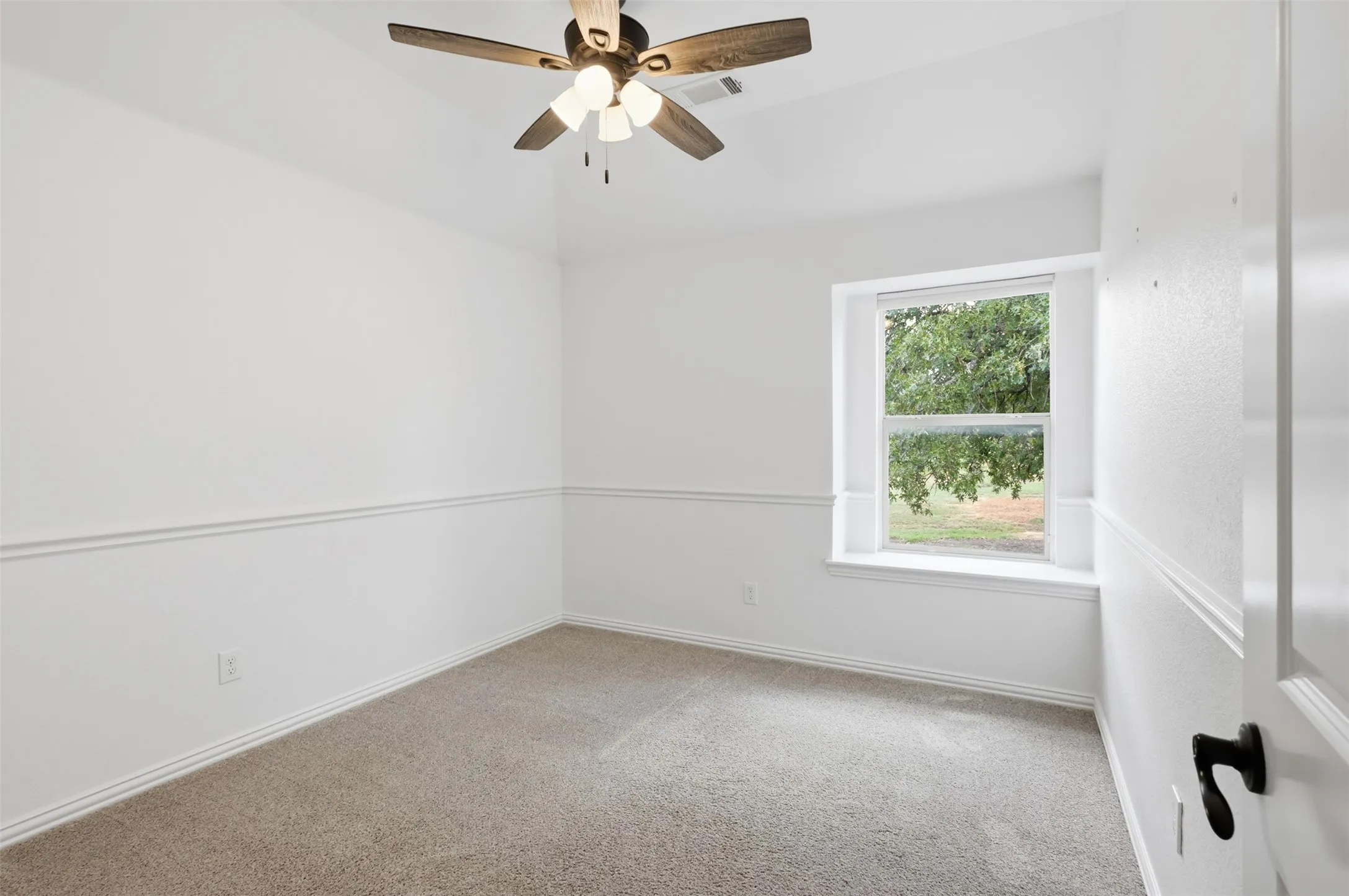 Neutral-toned room featuring a vaulted ceiling, ceiling fan with integrated lighting, wall-mounted chair rail molding, and a deep-set window