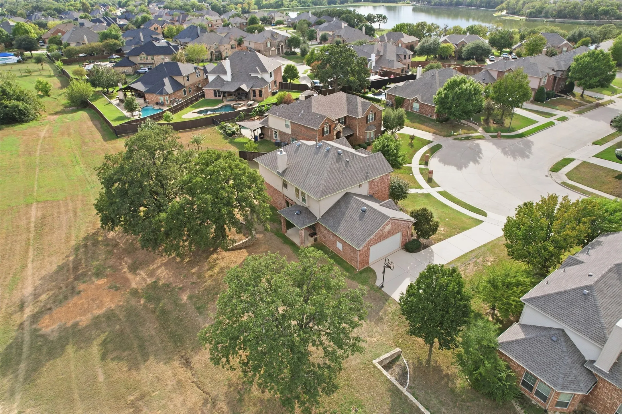 Two-story brick and masonry exterior featuring an attached two-car garage, steep-pitched roof, stone chimney, and expansive corner lot with mature trees
