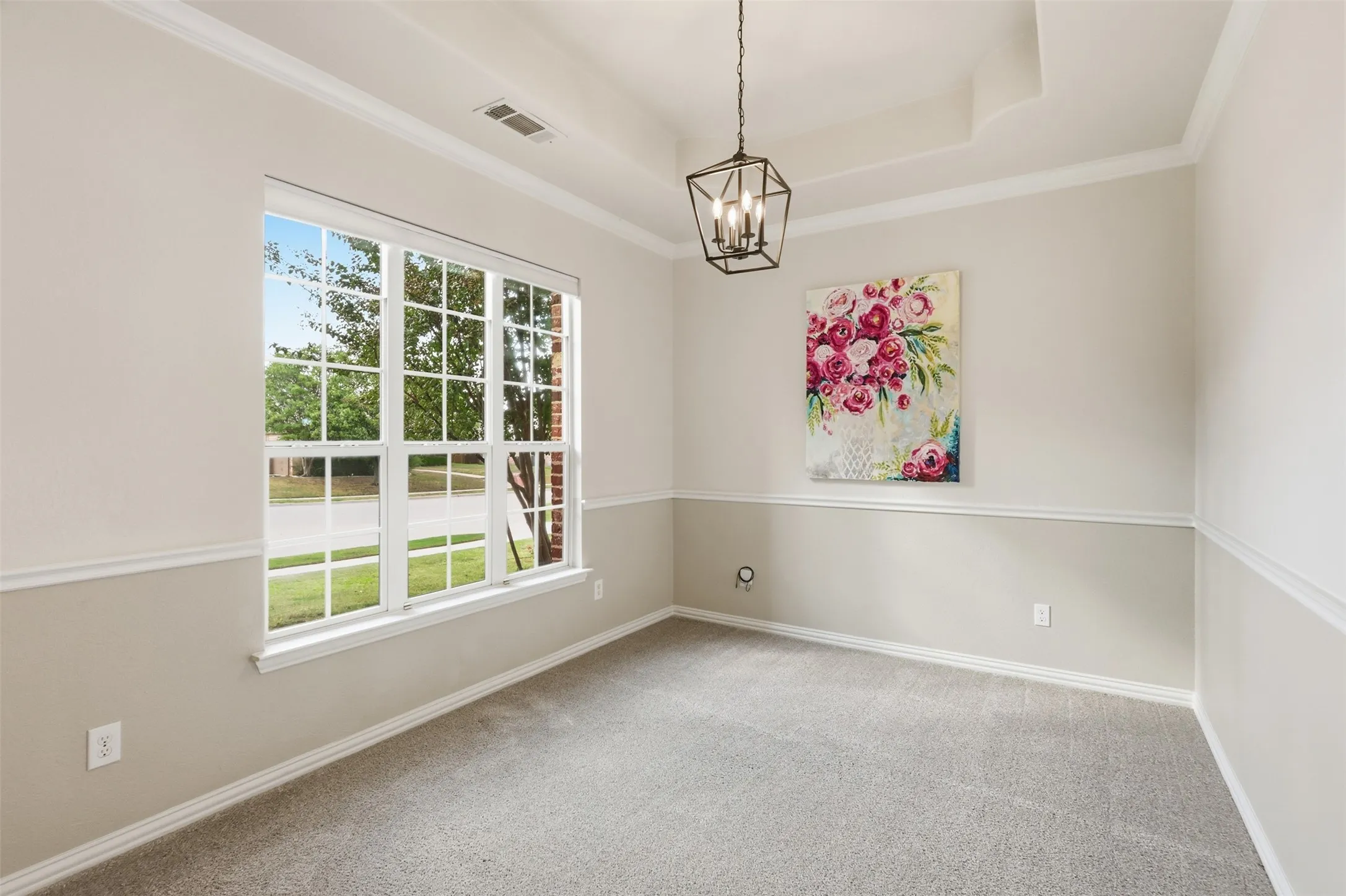 Tray ceiling, geometric metal pendant light, multi-pane window with grid pattern, and chair rail molding