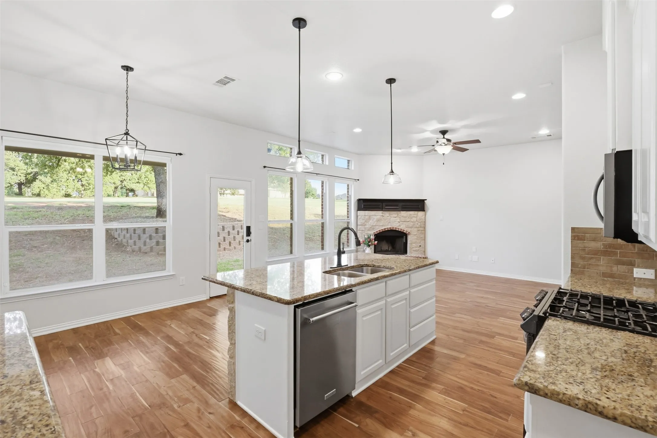 Kitchen featuring a center island with stone-finish countertops, stainless steel dishwasher, wood-finish flooring, recessed lighting, and a corner fireplace with a masonry surround