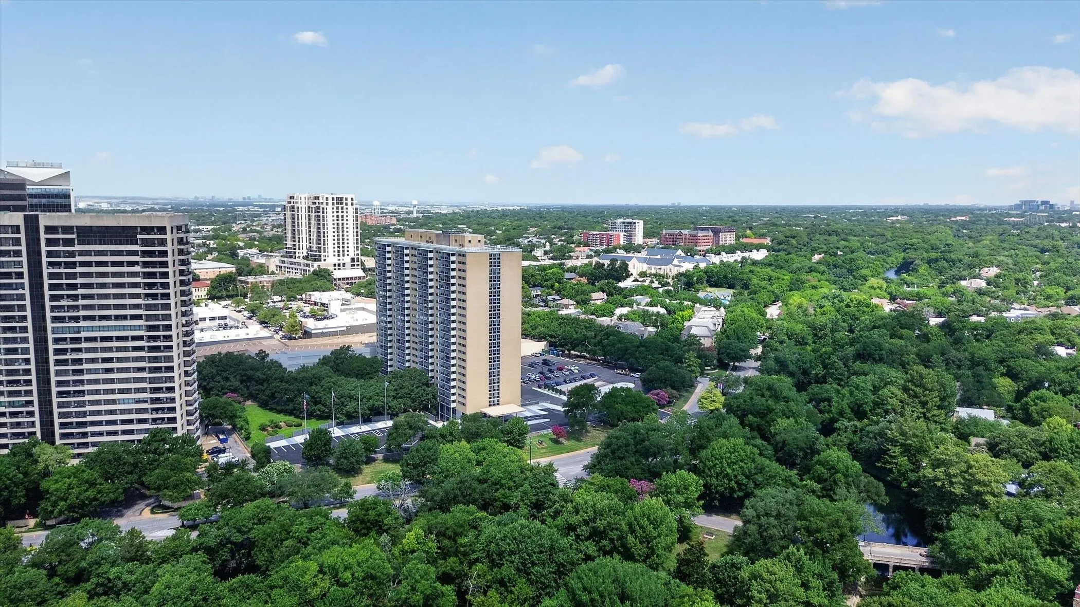 Aerial perspective featuring high-rise architecture, paved surface parking, and mature tree canopy