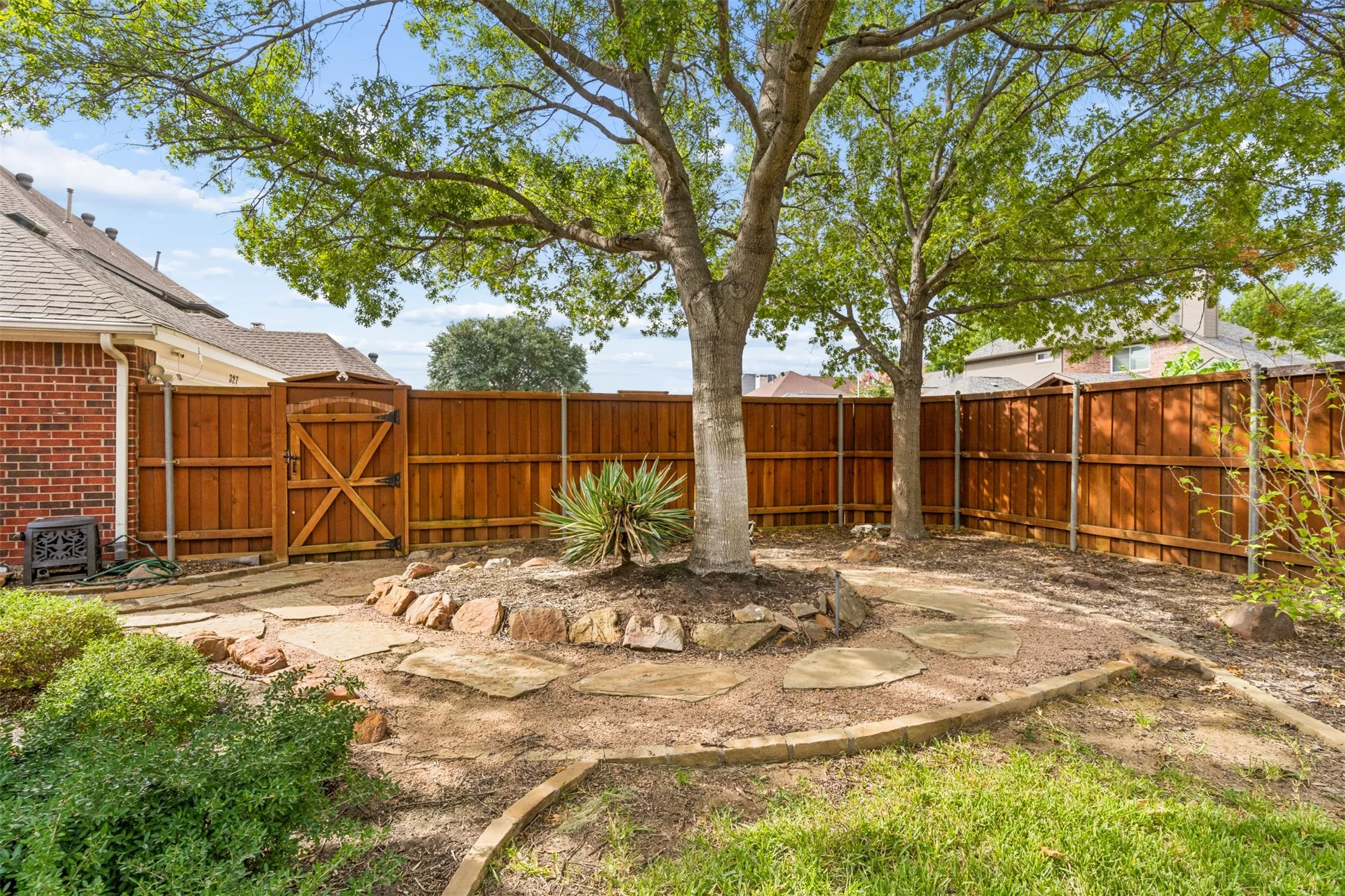 Backyard featuring a wood privacy fence, stone-bordered landscaping, mature trees, and natural stone hardscaping