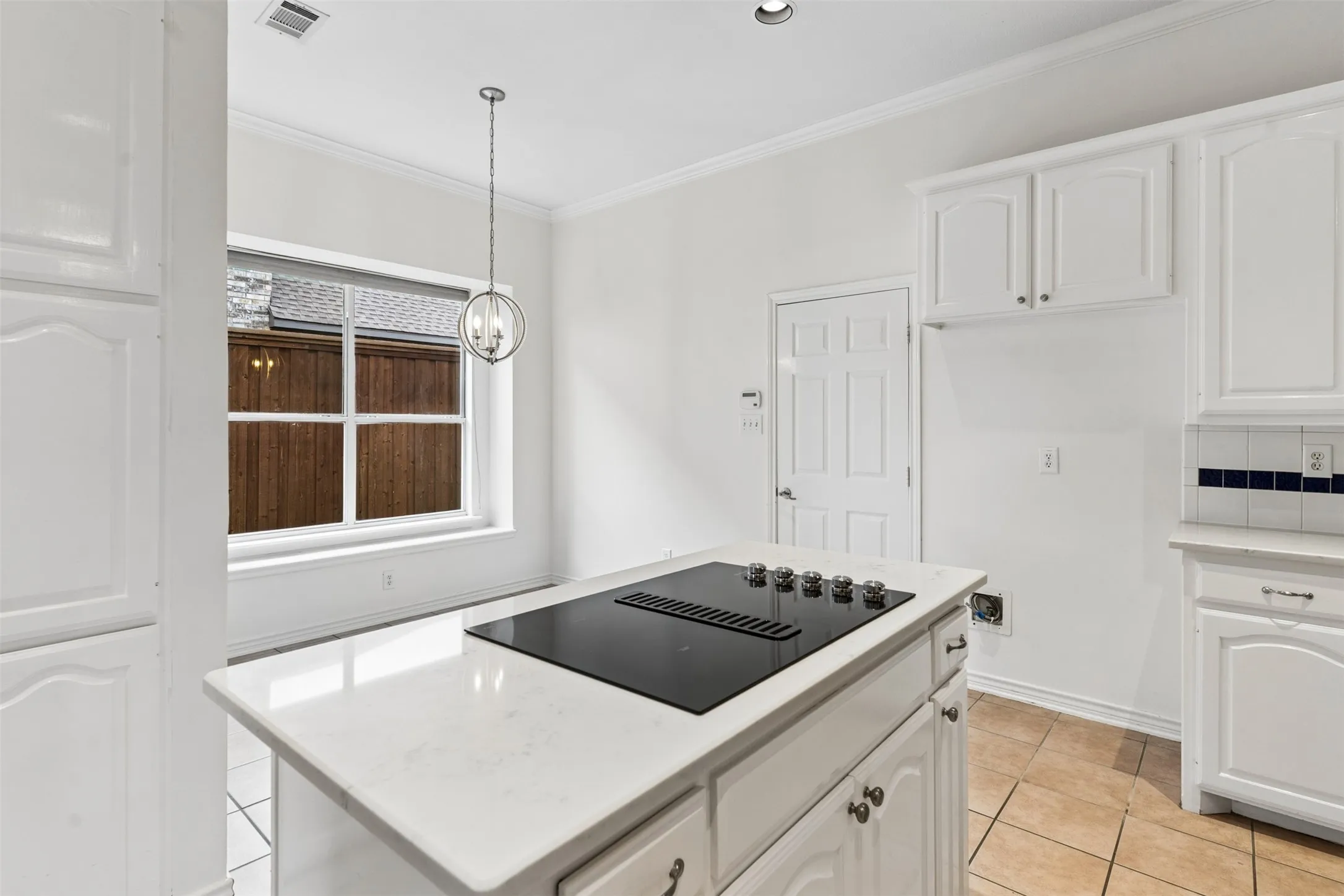 Kitchen island with a light-toned solid surface countertop and built-in electric cooktop, white cabinetry, tile flooring, and a multi-light pendant fixture