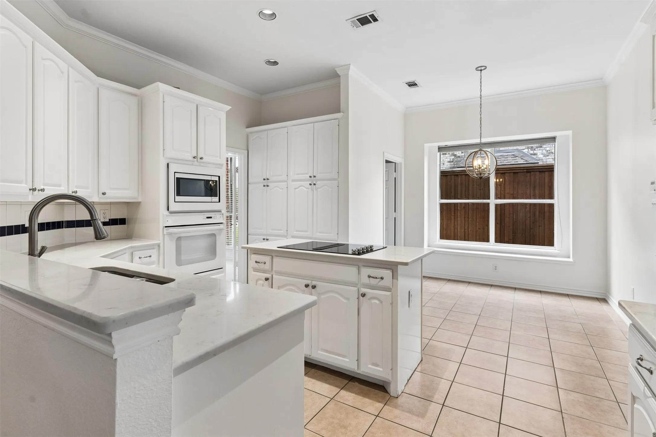 Kitchen featuring white cabinetry, stone-finish countertops, a center island with a built-in cooktop, integrated wall oven and microwave, and tile flooring