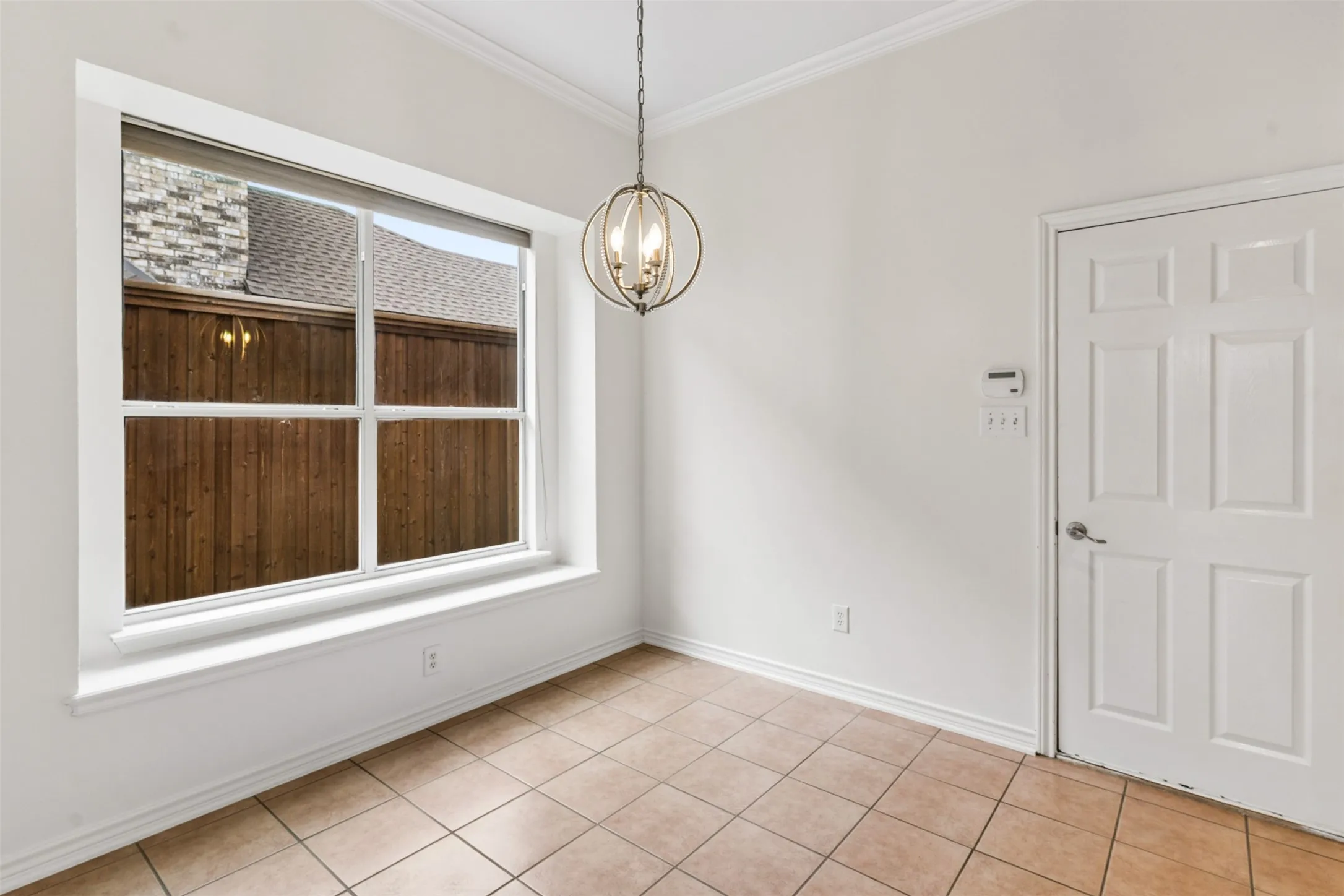 Large window featuring a deep sill, spherical metal-frame chandelier, neutral tile flooring, and a six-panel interior door