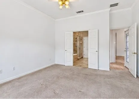 Room featuring neutral carpeting, crown molding, a ceiling fan with integrated lighting, and double-panel entry doors