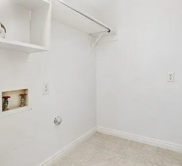 Laundry hookups featuring recessed plumbing valves, overhead built-in shelving, a hanging rod, and tile flooring