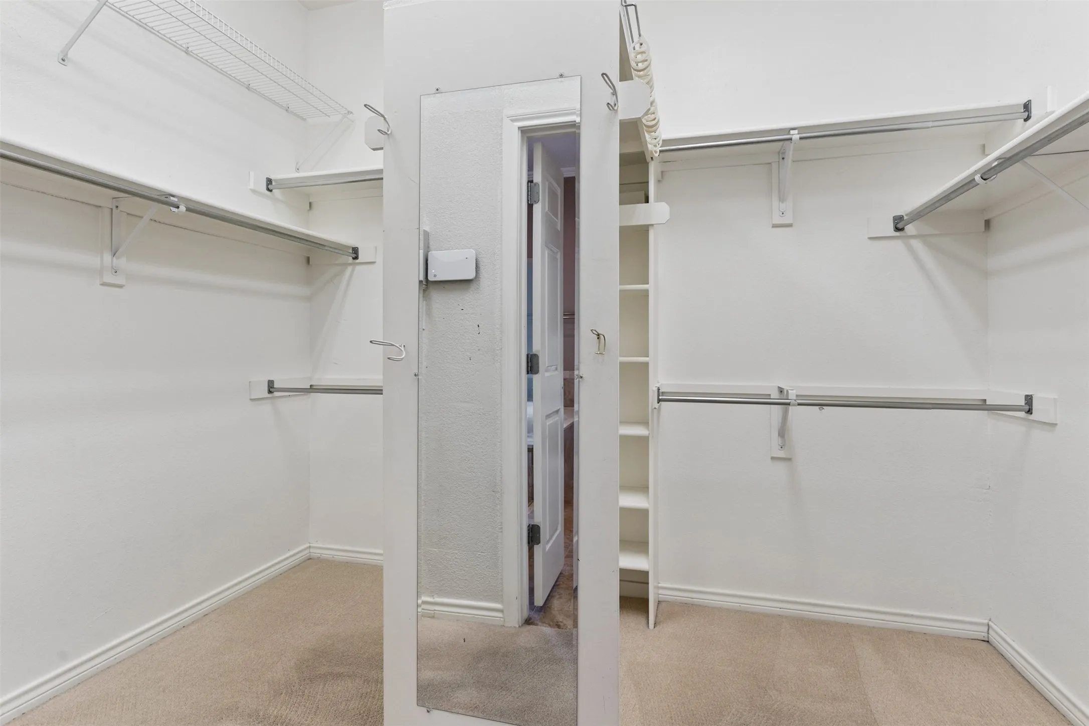 Walk-in closet featuring tiered metal garment rods, upper wire shelving, built-in vertical storage cabinetry, and a full-length wall-mounted mirror