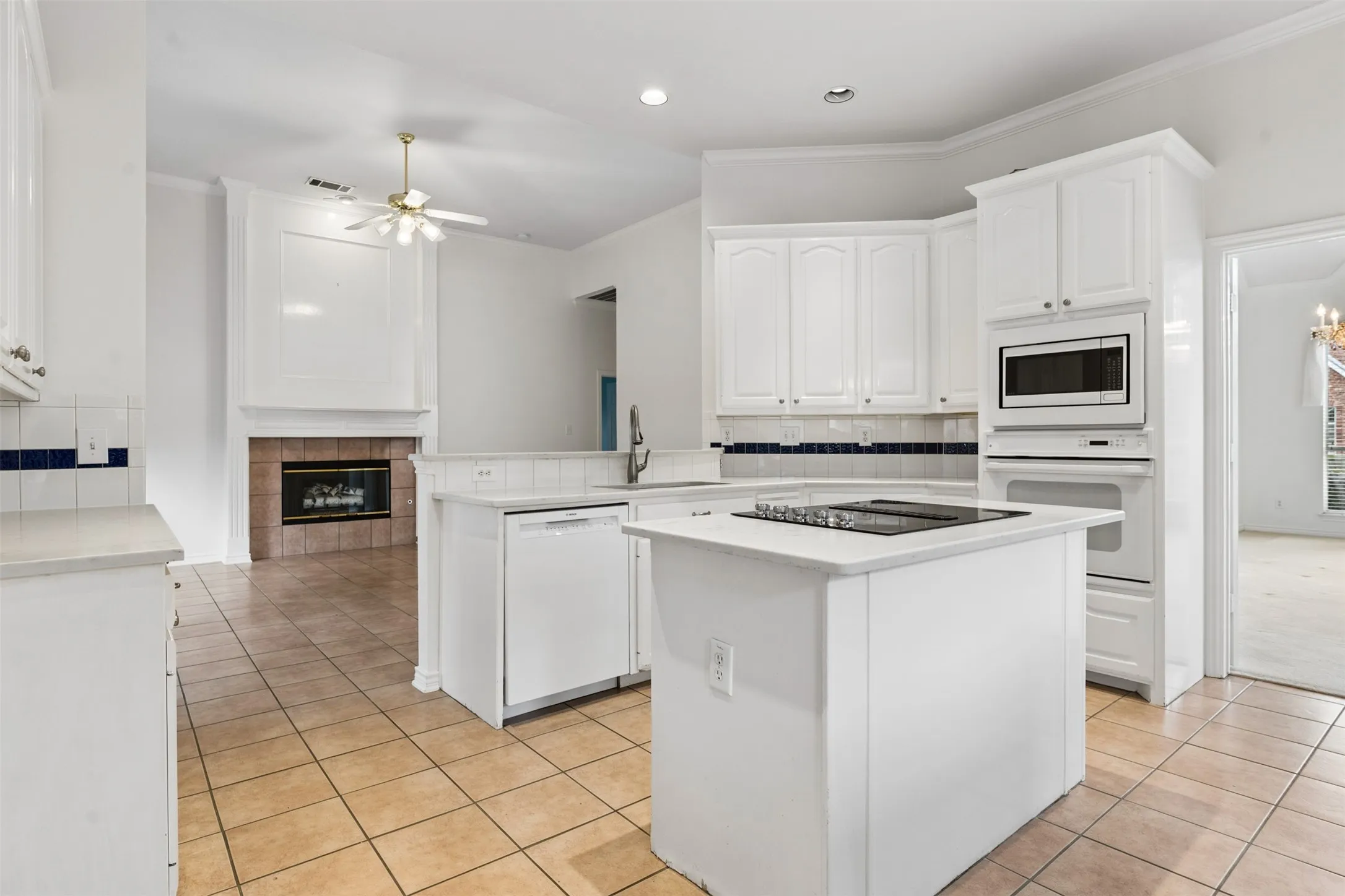 Kitchen featuring white cabinetry, center island with an integrated cooktop, built-in wall oven and microwave, ceramic tile flooring, and a fireplace with tile surround
