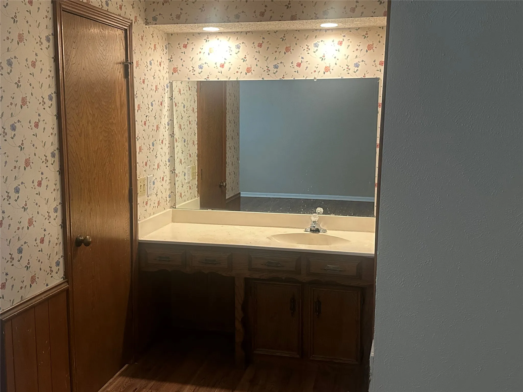 Vanity featuring wood cabinetry, integrated basin, countertop, and a large-format mirror with recessed lighting