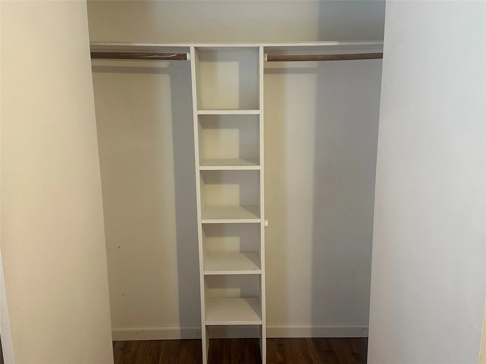 Closet featuring built-in vertical shelving, dual clothing rods, and wood-finish flooring