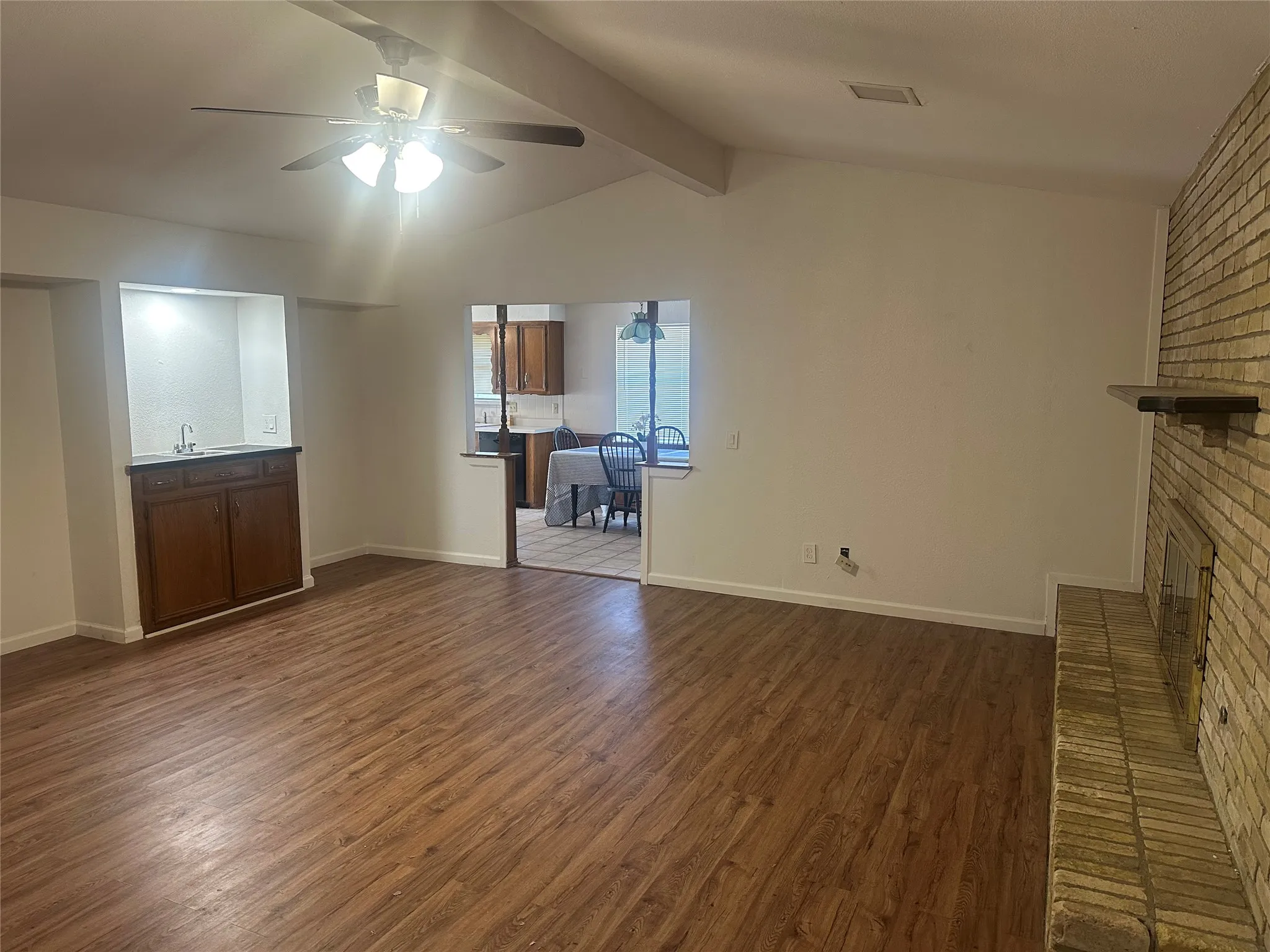 Vaulted ceiling with exposed beam, wood-finish flooring, full-height masonry fireplace, and built-in wet bar featuring dark wood cabinetry and a sink