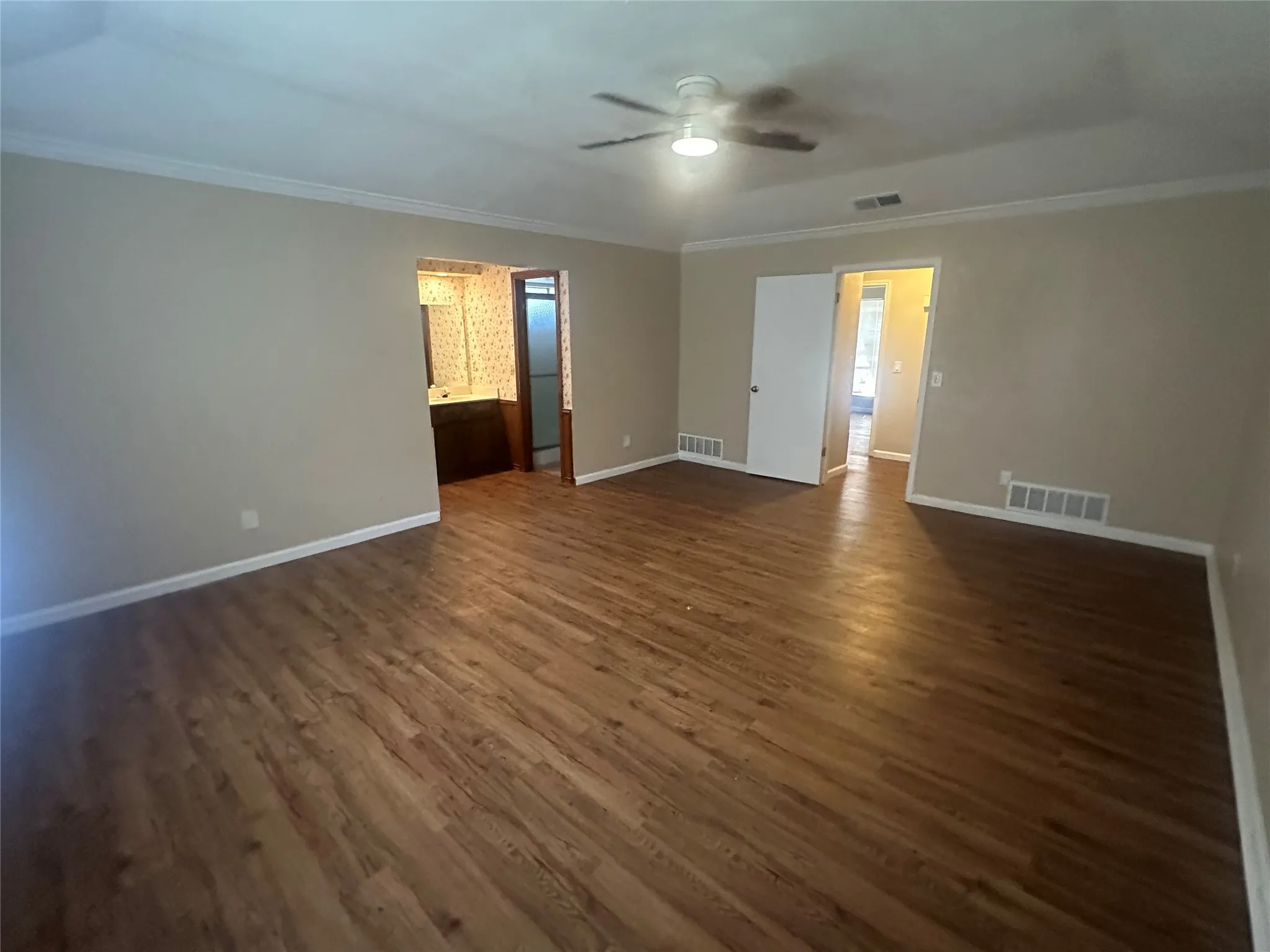 Spacious room featuring wood-finish flooring, crown molding, and a central ceiling fan
