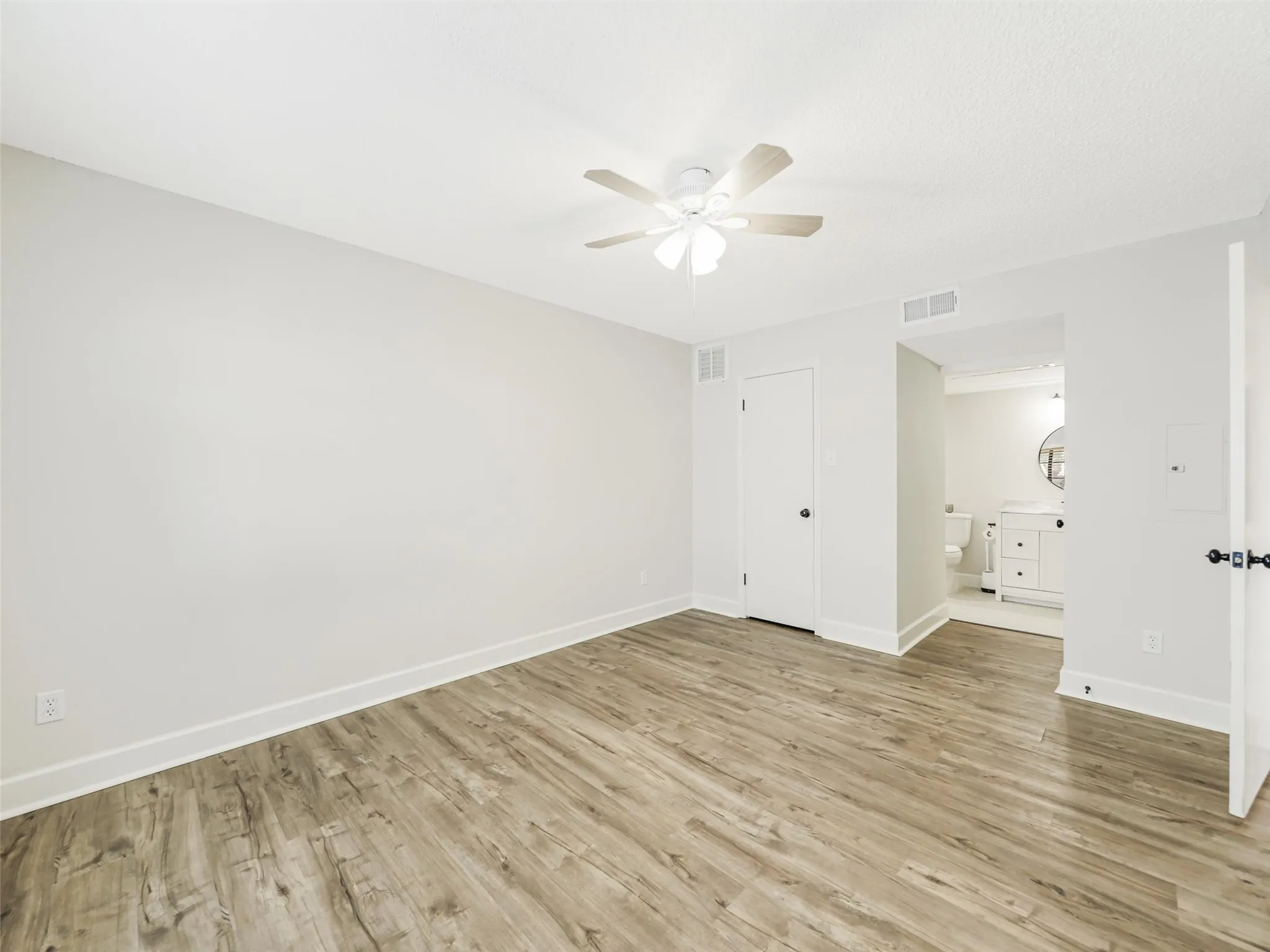 Neutral wall tones, wood-finish flooring, and a ceiling-mounted light fixture with fan
