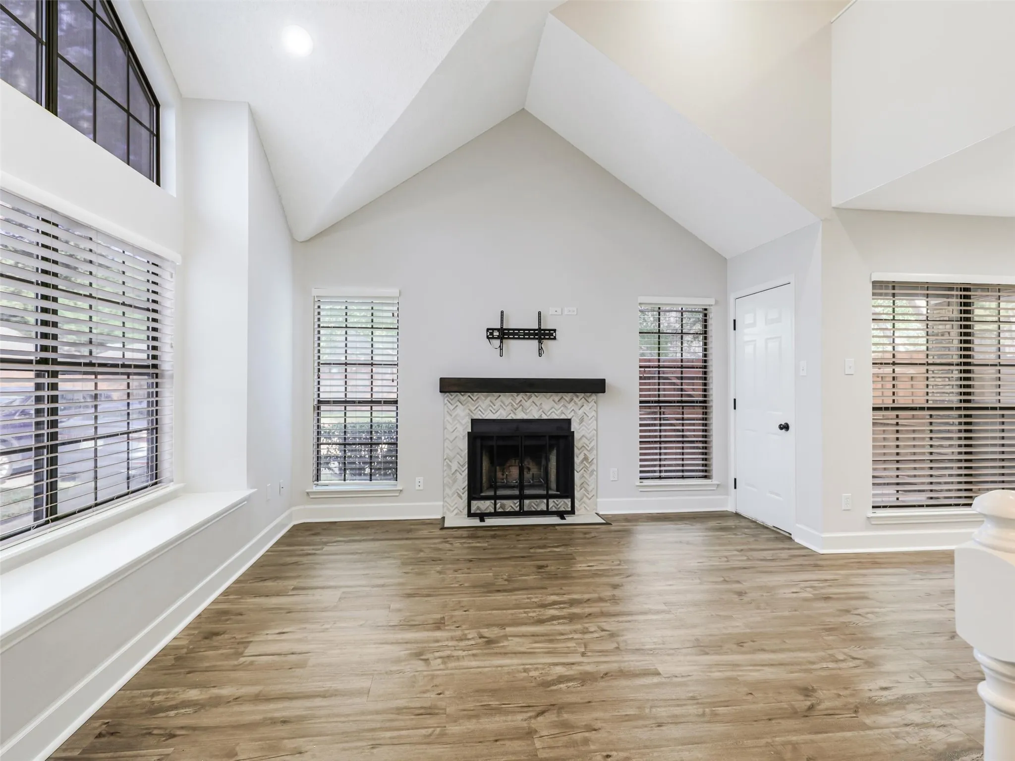Vaulted ceilings featuring a fireplace with a chevron-pattern tile surround and a dark wood mantel, wood-finish flooring, and expansive windows with built-in window seating