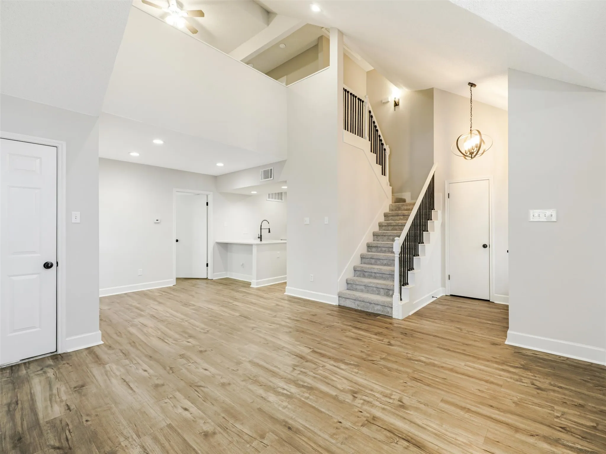 Vaulted ceilings with recessed lighting, wood-finish flooring, staircase with a matte black railing, orb-style pendant lighting, and an integrated wet bar