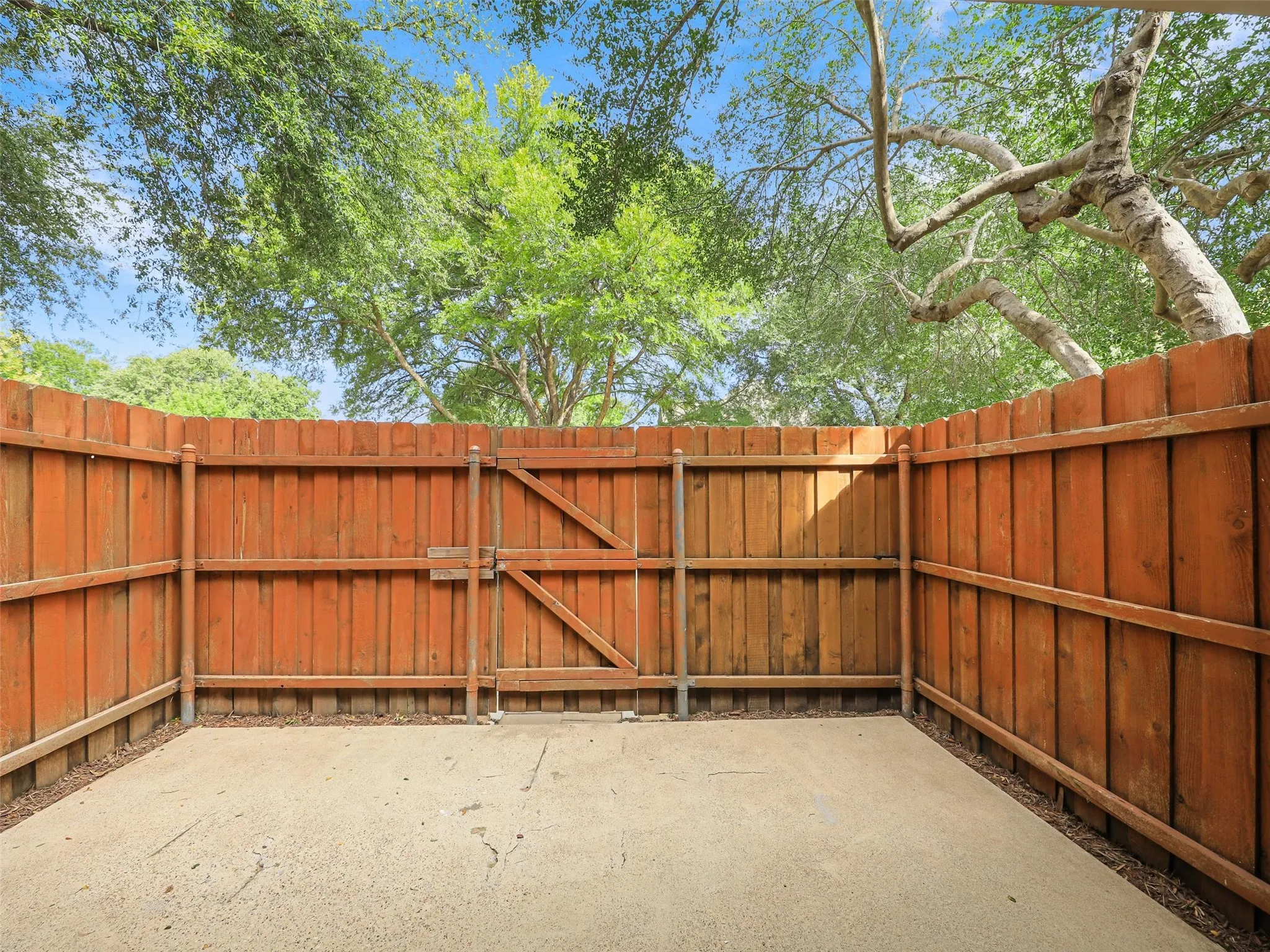 Concrete patio enclosed by a wood privacy fence featuring a functional access gate and mature tree canopy