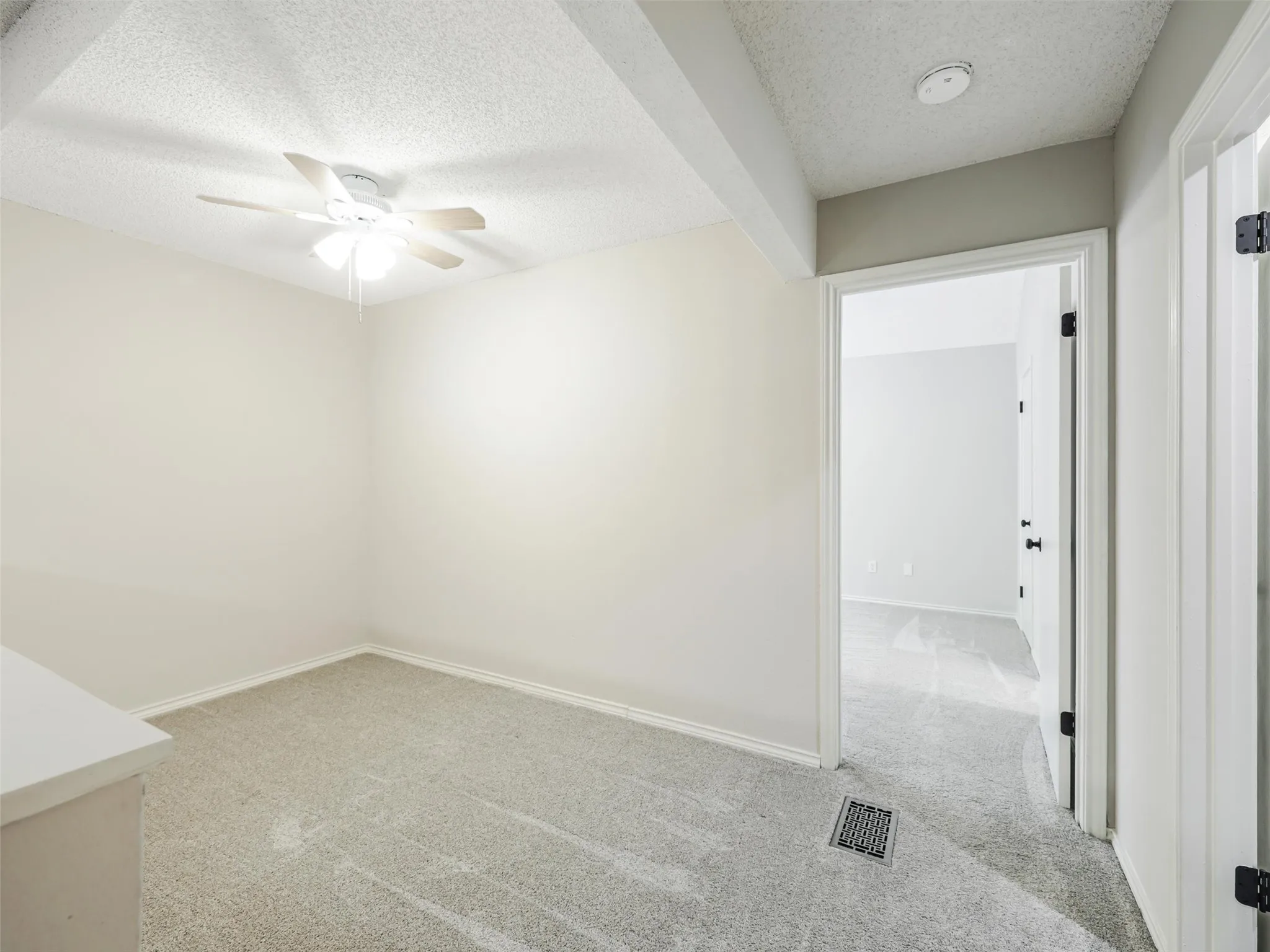 Neutral-toned interior space featuring wall-to-wall carpeting, a ceiling fan with integrated lighting, and a doorway with a hollow-core door