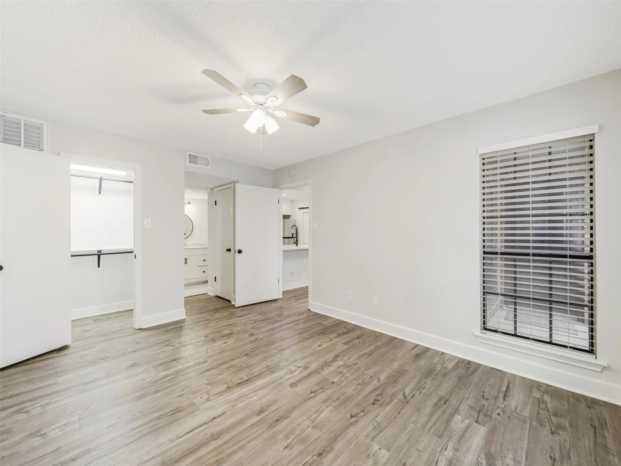 Room featuring wood-finish flooring, a ceiling fan with integrated lighting, a window with horizontal blinds, and built-in closet shelving