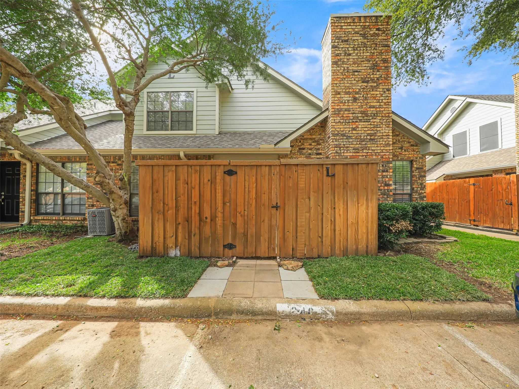 Exterior elevation featuring a brick and horizontal siding facade, a prominent brick chimney, and a wooden privacy fence with a stone-paved walkway