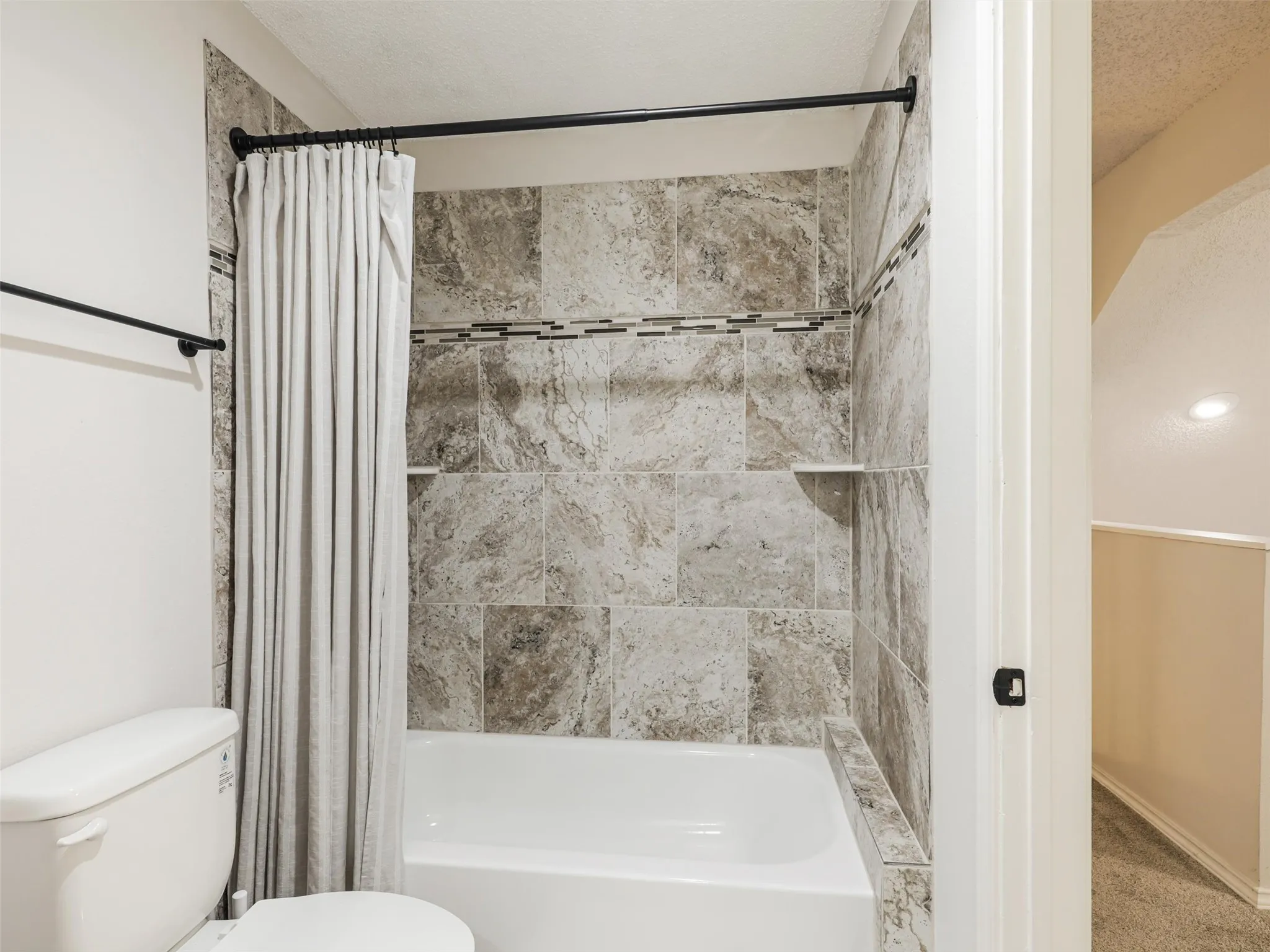 Full-size bathtub with patterned tile surround, integrated recessed shelving, and a decorative mosaic accent border