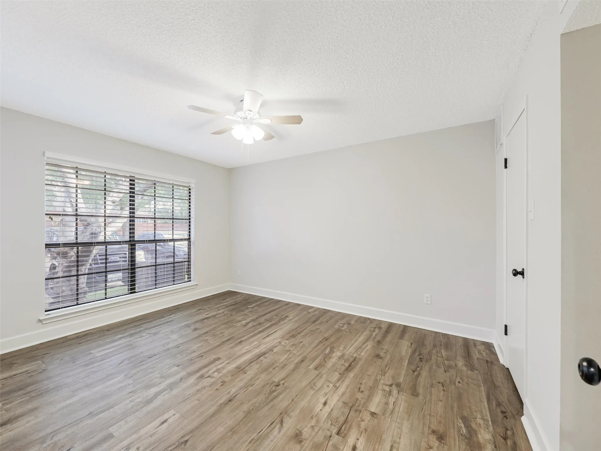 Room featuring wood-finish flooring, a neutral color palette, a ceiling fan with integrated lighting, and a multi-pane window with horizontal blinds
