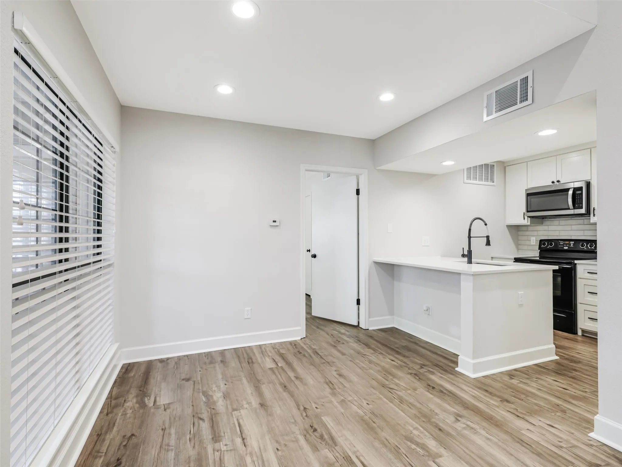 Wood-finish flooring, recessed lighting, white cabinetry, matte black hardware, and a breakfast bar