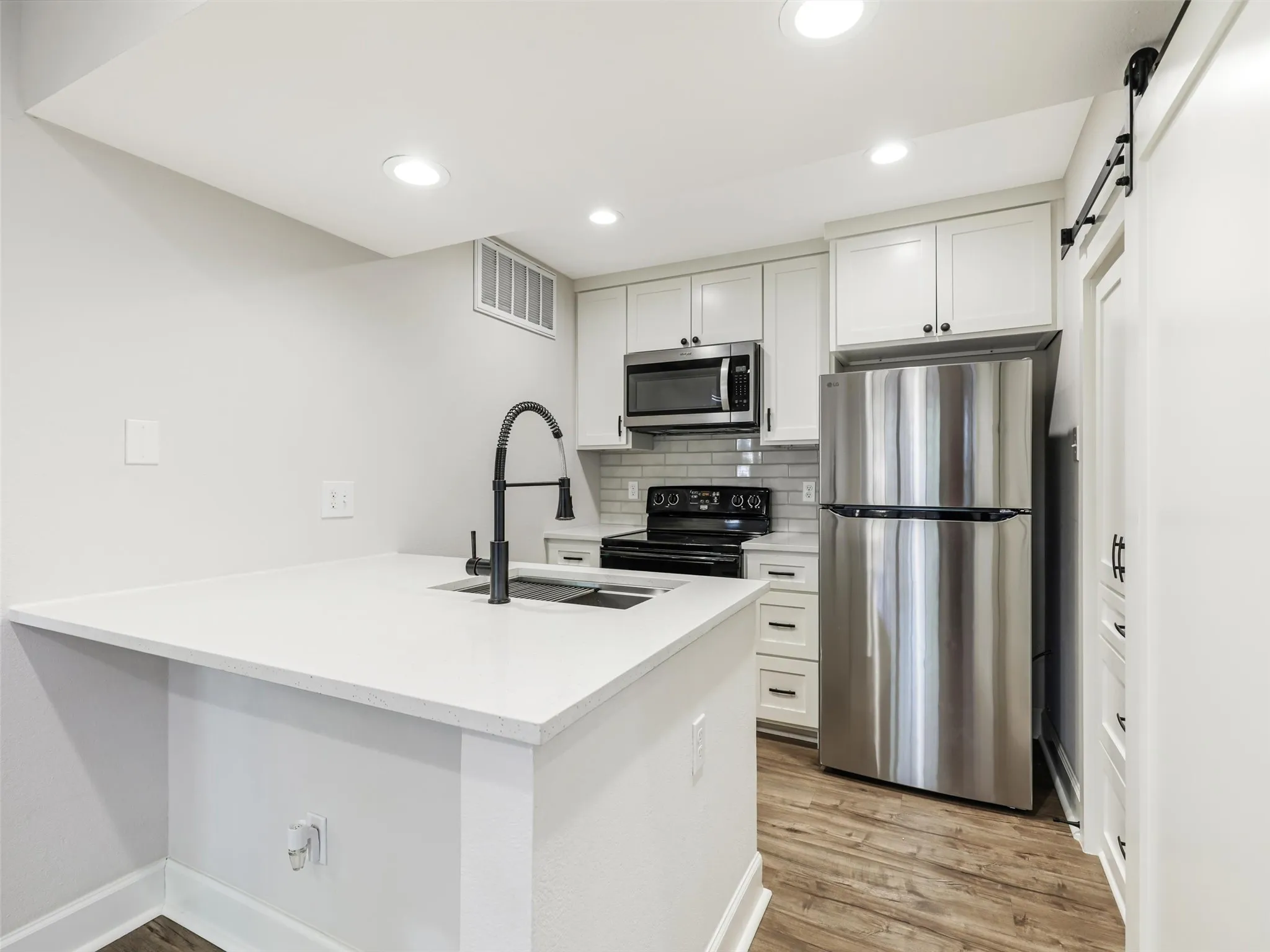 Kitchen featuring white shaker-style cabinetry, solid-surface countertops, stainless steel appliances, matte black plumbing fixtures, and wood-finish flooring