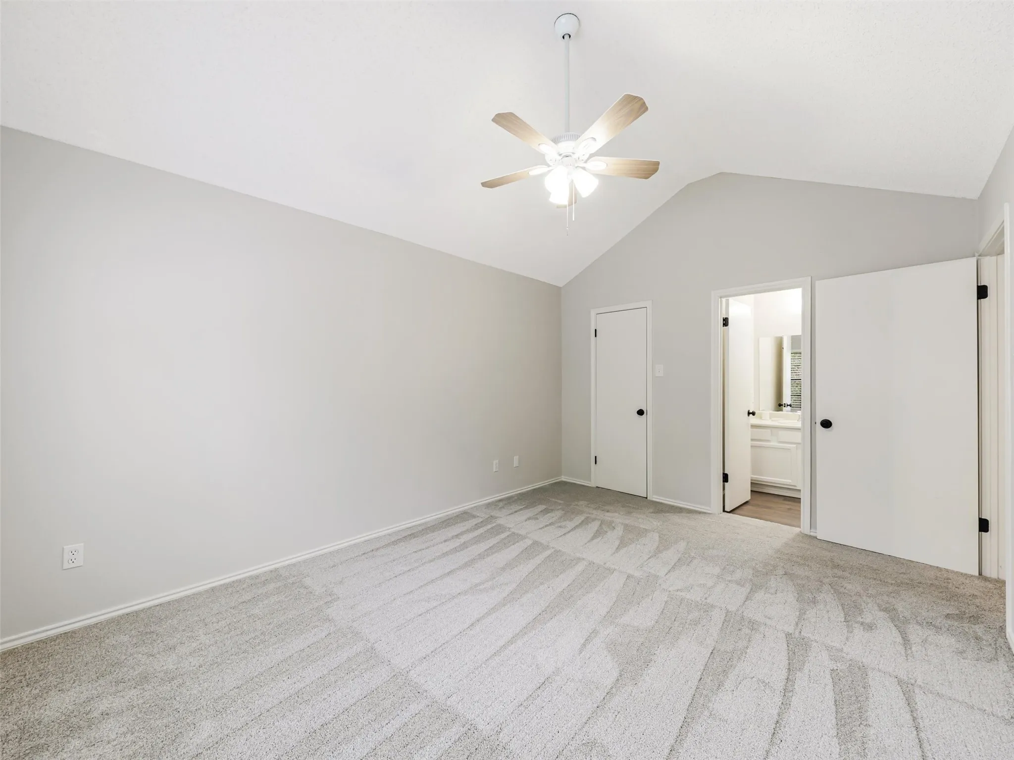 Vaulted ceiling featuring a central lighted ceiling fan, neutral wall tones, and neutral-toned carpeting