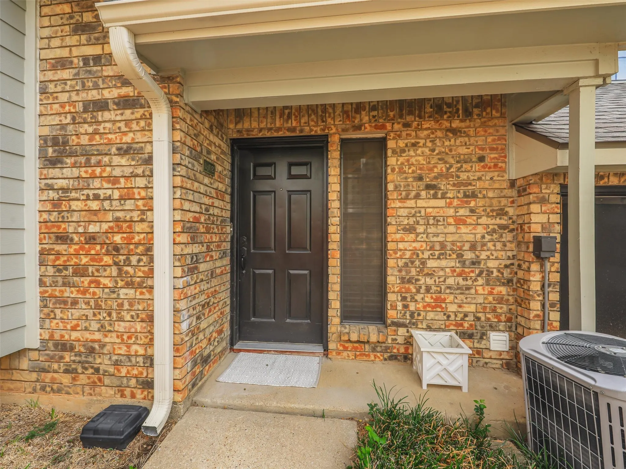 Exterior entryway featuring a multi-tone brick facade, six-panel dark entry door, sidelight window, and a covered porch with concrete flooring