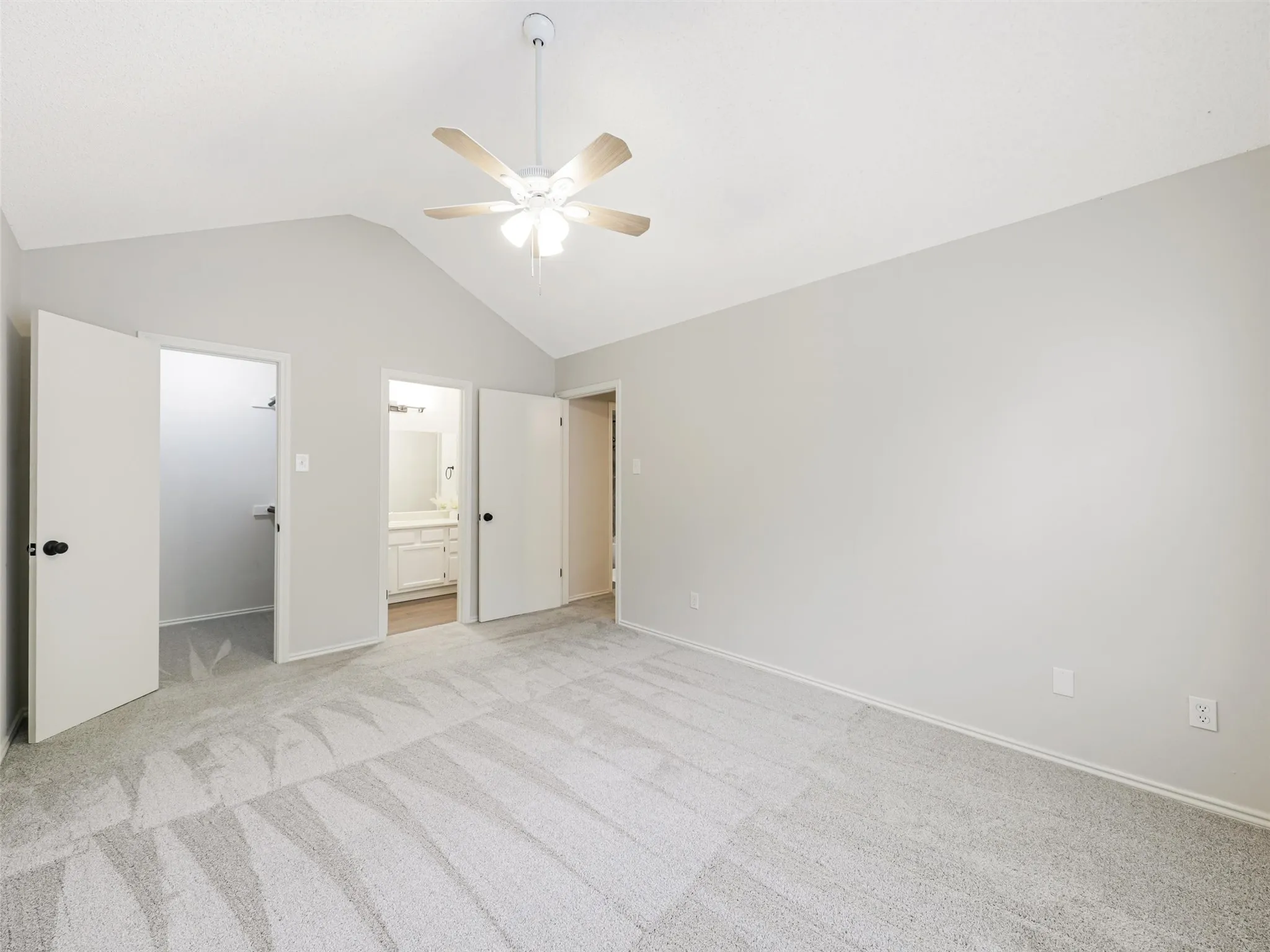 Vaulted ceilings featuring a central overhead fan with light fixture, neutral wall finishes, and carpeting