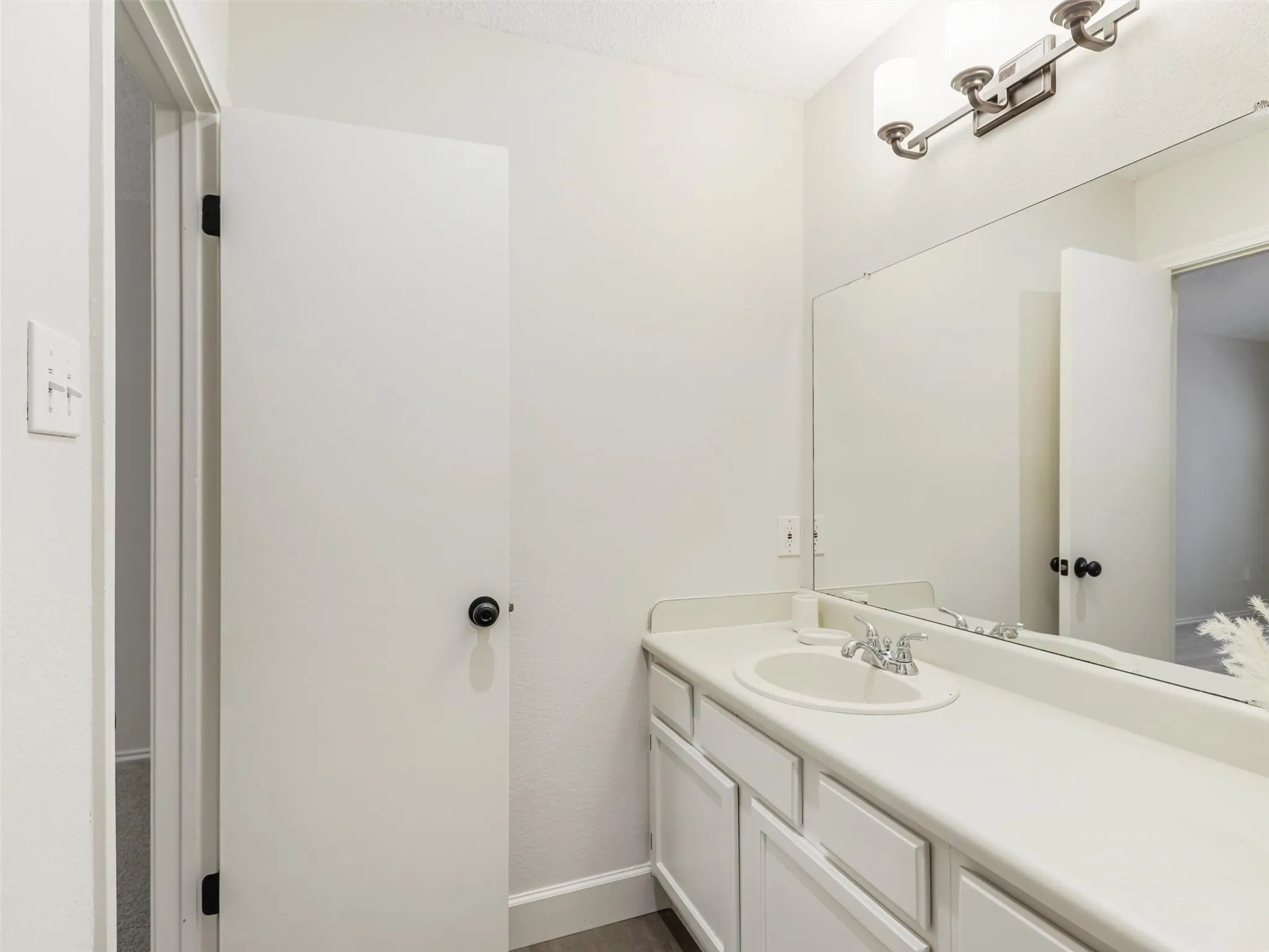 Vanity with a solid-surface countertop and integrated basin, large wall-mounted mirror, and multi-bulb vanity light fixture