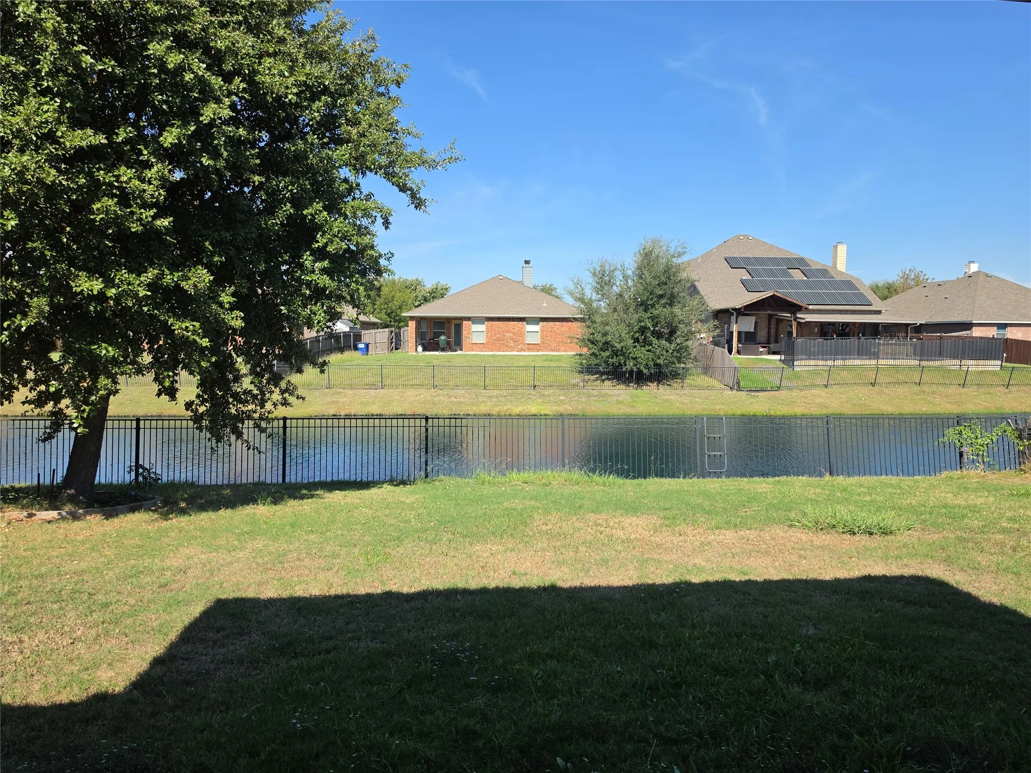 Backyard featuring a grass lawn, mature tree, metal perimeter fencing, and waterfront access