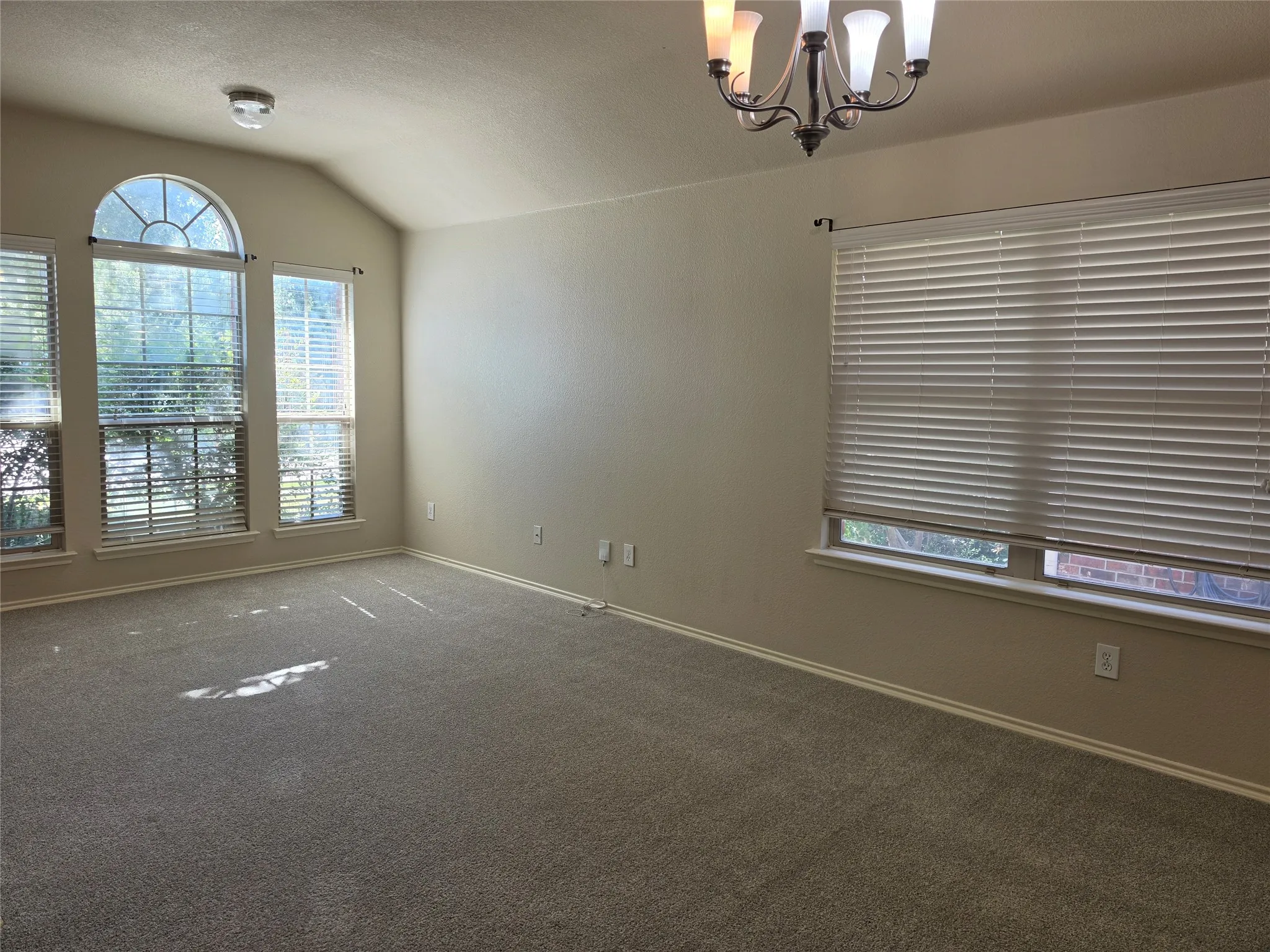Vaulted ceilings, arched windows, multi-light chandelier, and horizontal window blinds