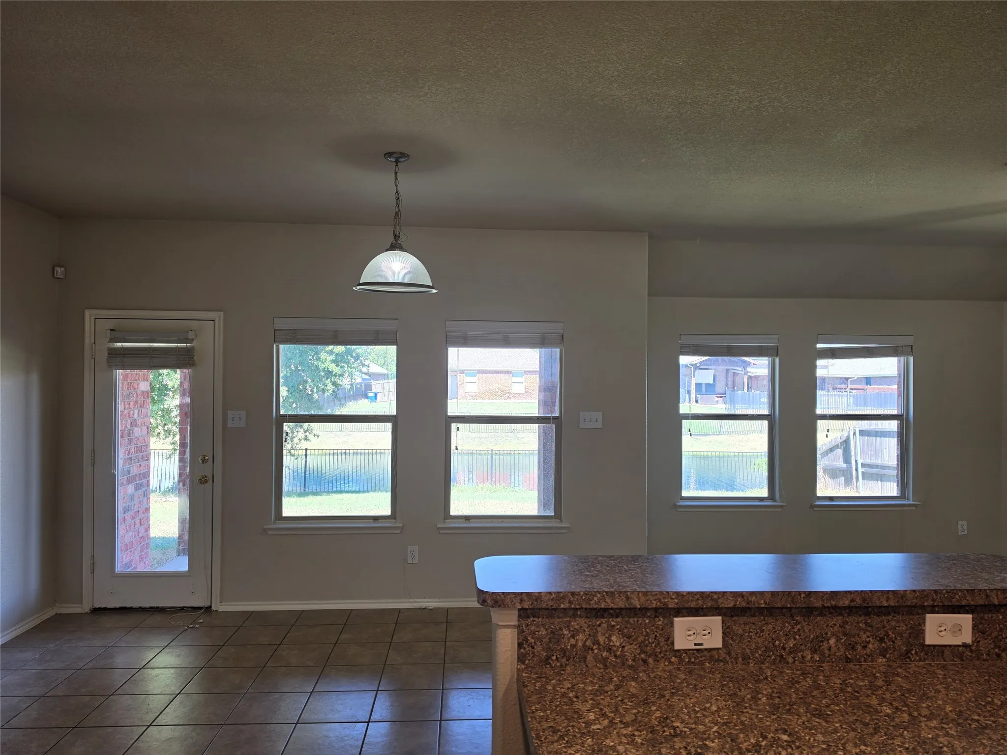Ceramic tile flooring, stone-finish countertops, single-pendant ceiling light, and multiple large windows with exterior access via a glass-paneled door