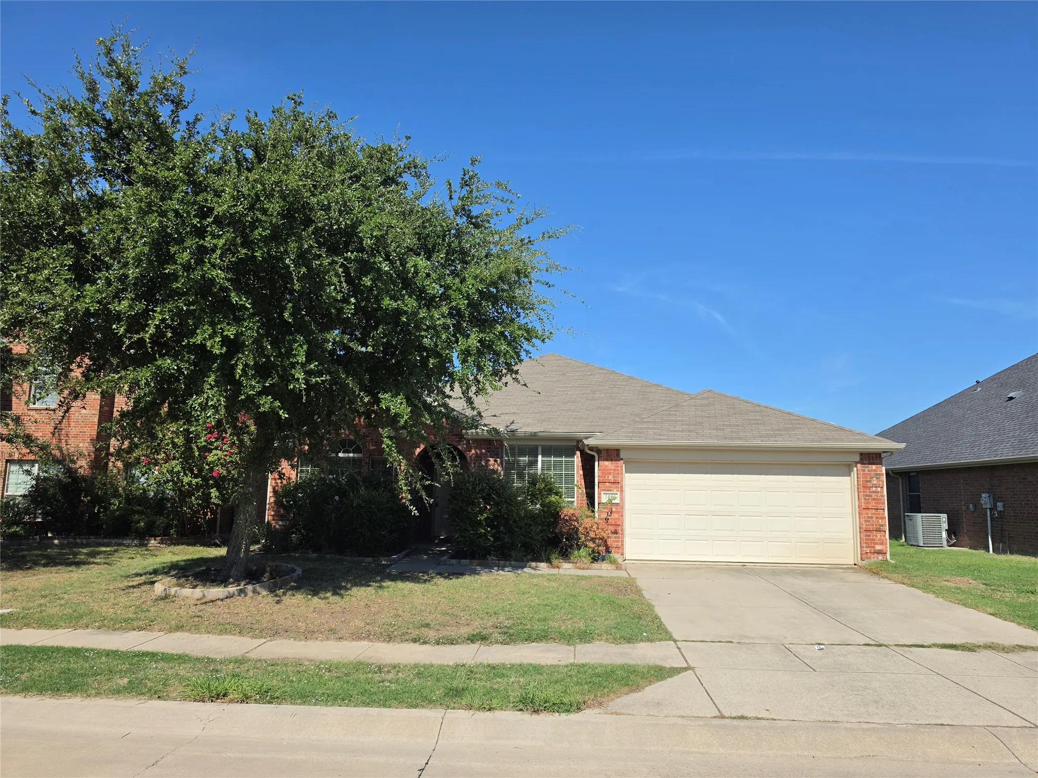Brick exterior facade, attached two-car garage, concrete driveway, and mature landscaping