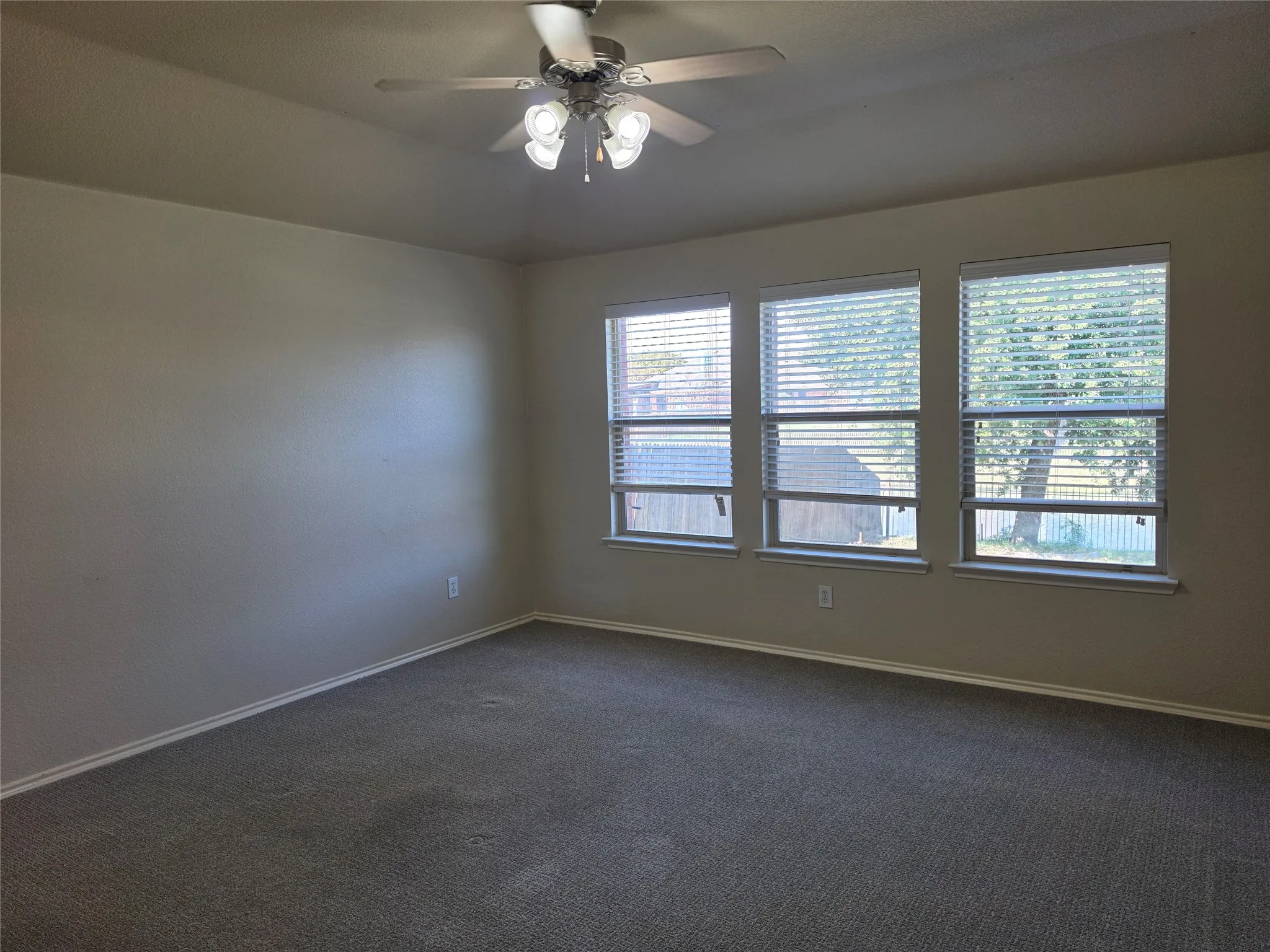 Tray ceiling featuring a central multi-light ceiling fan, neutral wall tones, and three large windows with horizontal blinds