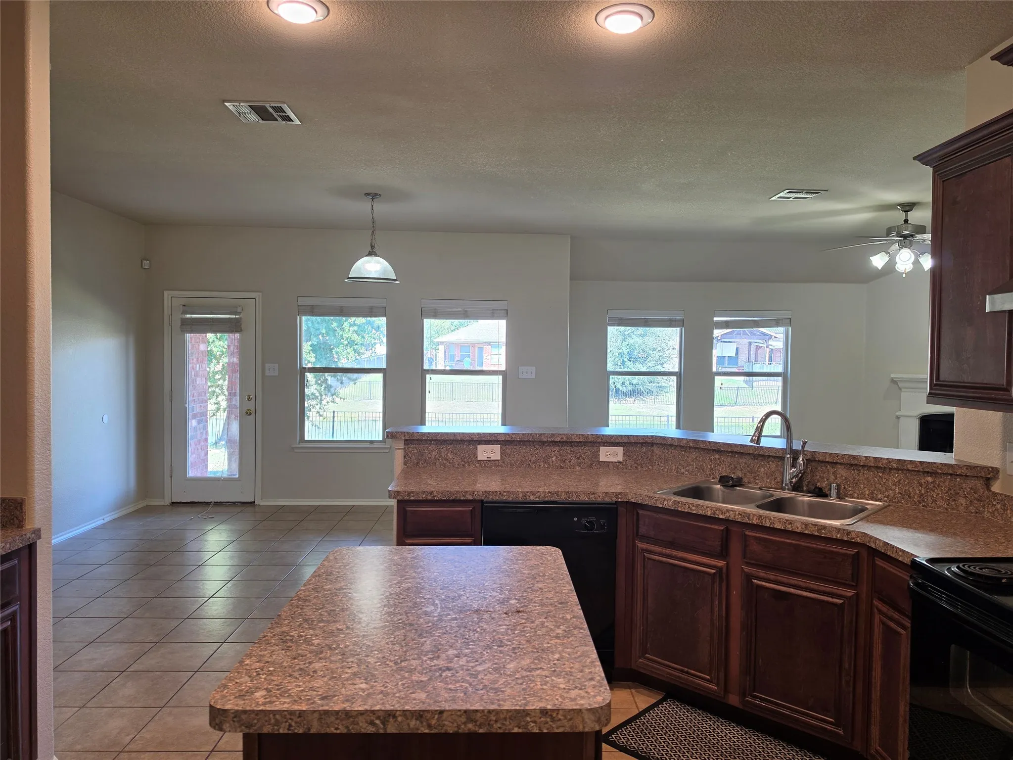 Kitchen featuring stained wood cabinetry, a central island, laminate countertops, a dual-basin stainless steel sink with a high-arch faucet, and tile flooring