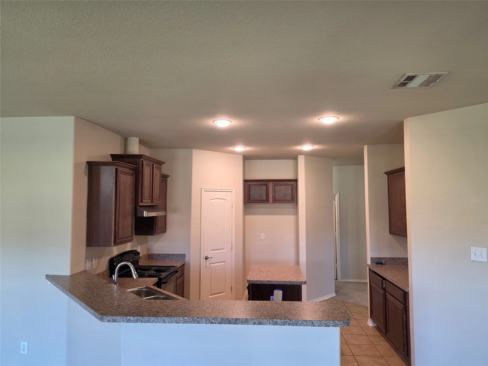 Kitchen featuring dark wood-finish cabinetry, stone-texture countertops, a peninsula breakfast bar with an undermount sink, and recessed lighting