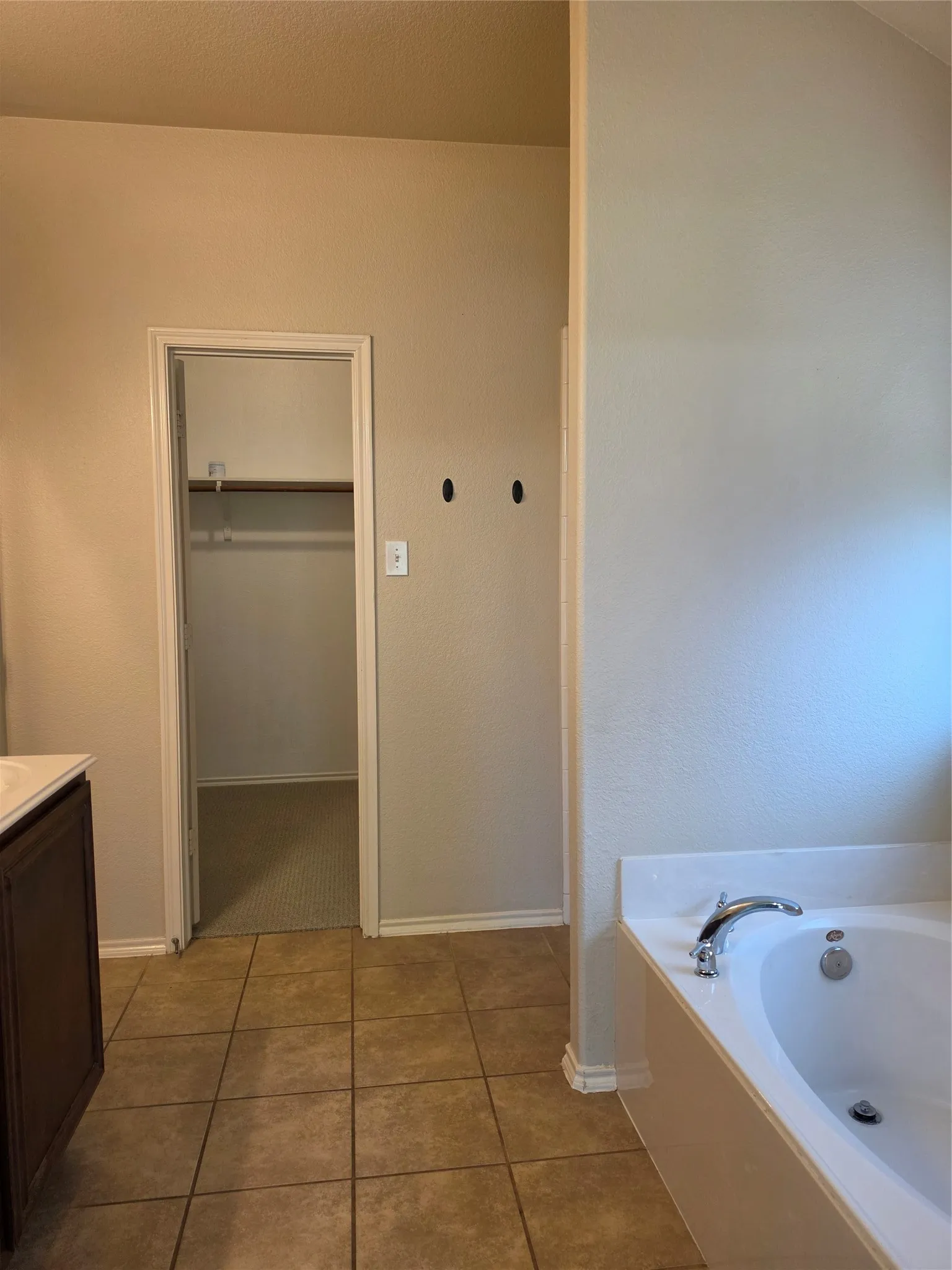 Deep soaking tub with a curved chrome faucet, tile flooring, dark wood cabinetry, and a walk-in closet with built-in shelving