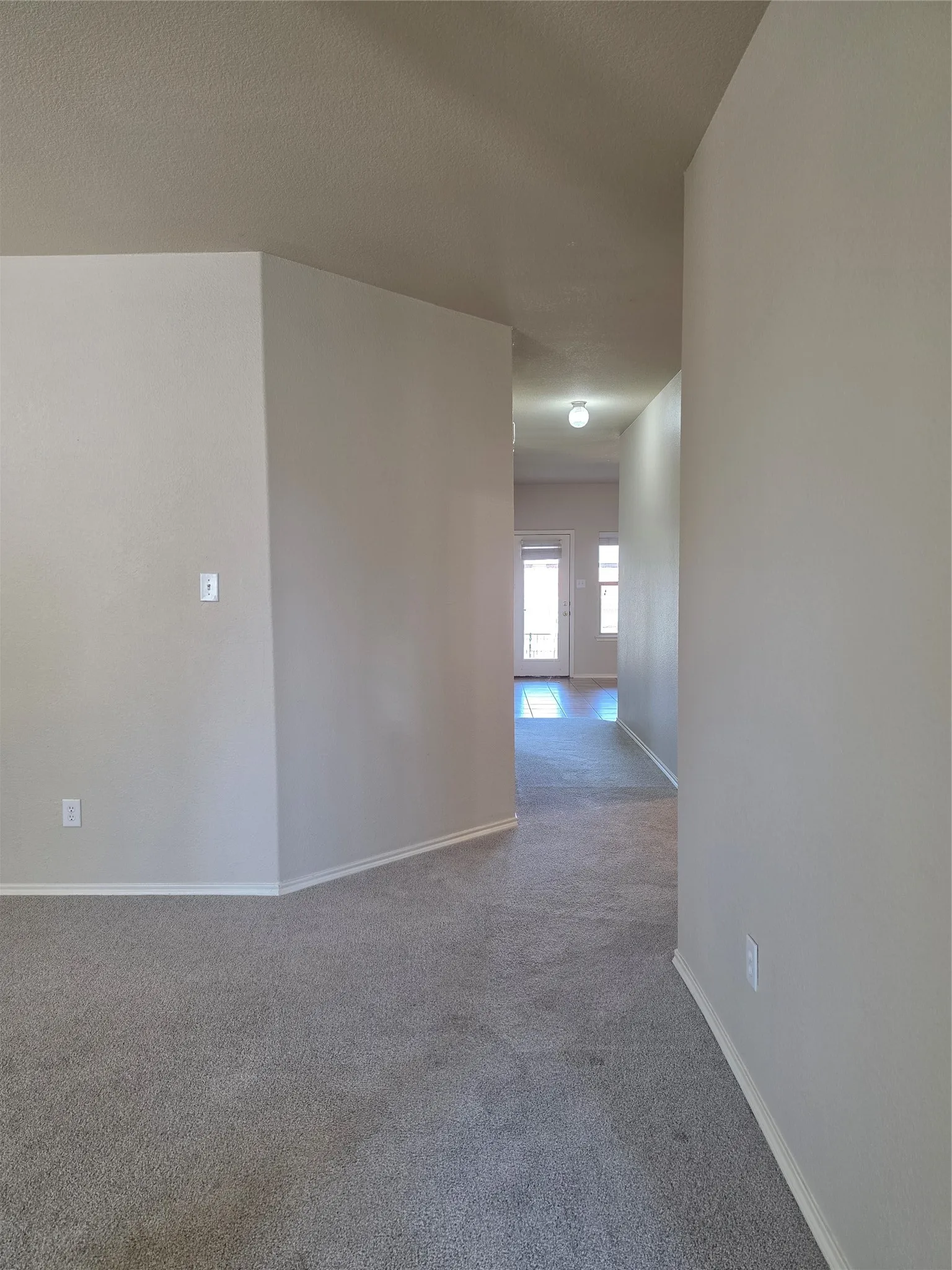 Neutral-toned interior featuring wall-to-wall carpeting, textured wall finish, and an exterior door with integrated glass