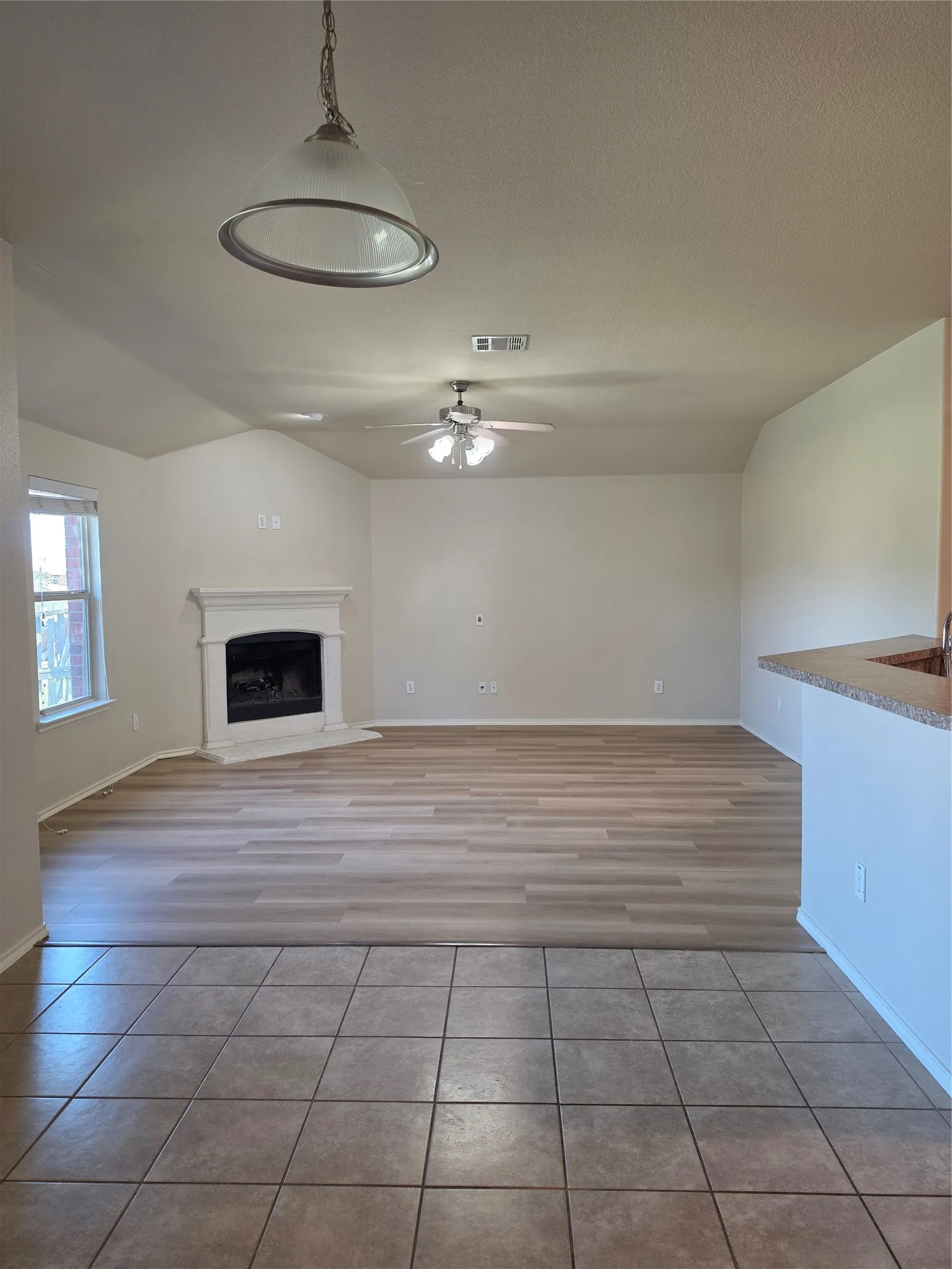 Living area featuring wood-finish flooring, a white-mantel fireplace, vaulted ceilings, and a ceiling fan with integrated lighting