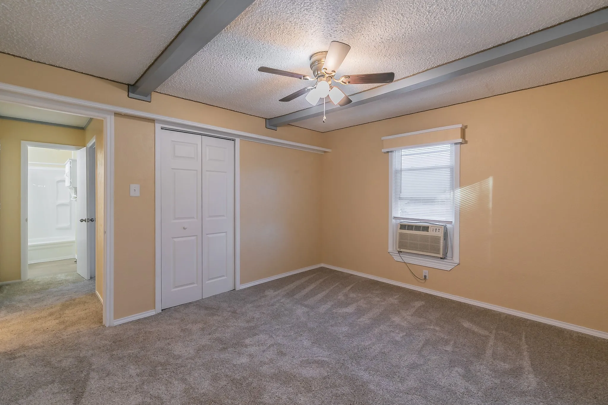 Unfurnished bedroom featuring carpet flooring, ceiling fan, a closet, and beamed ceiling