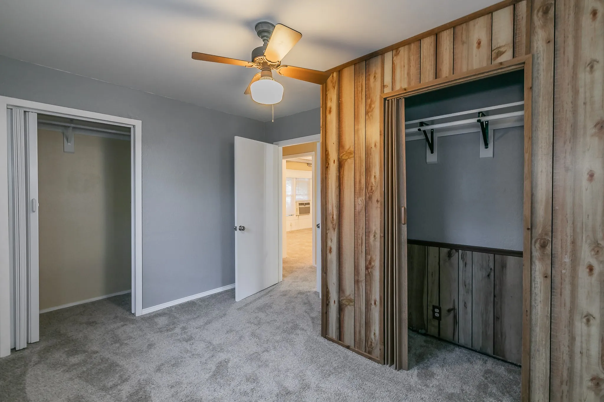 Unfurnished bedroom featuring ceiling fan, a closet, light colored carpet, and wood walls