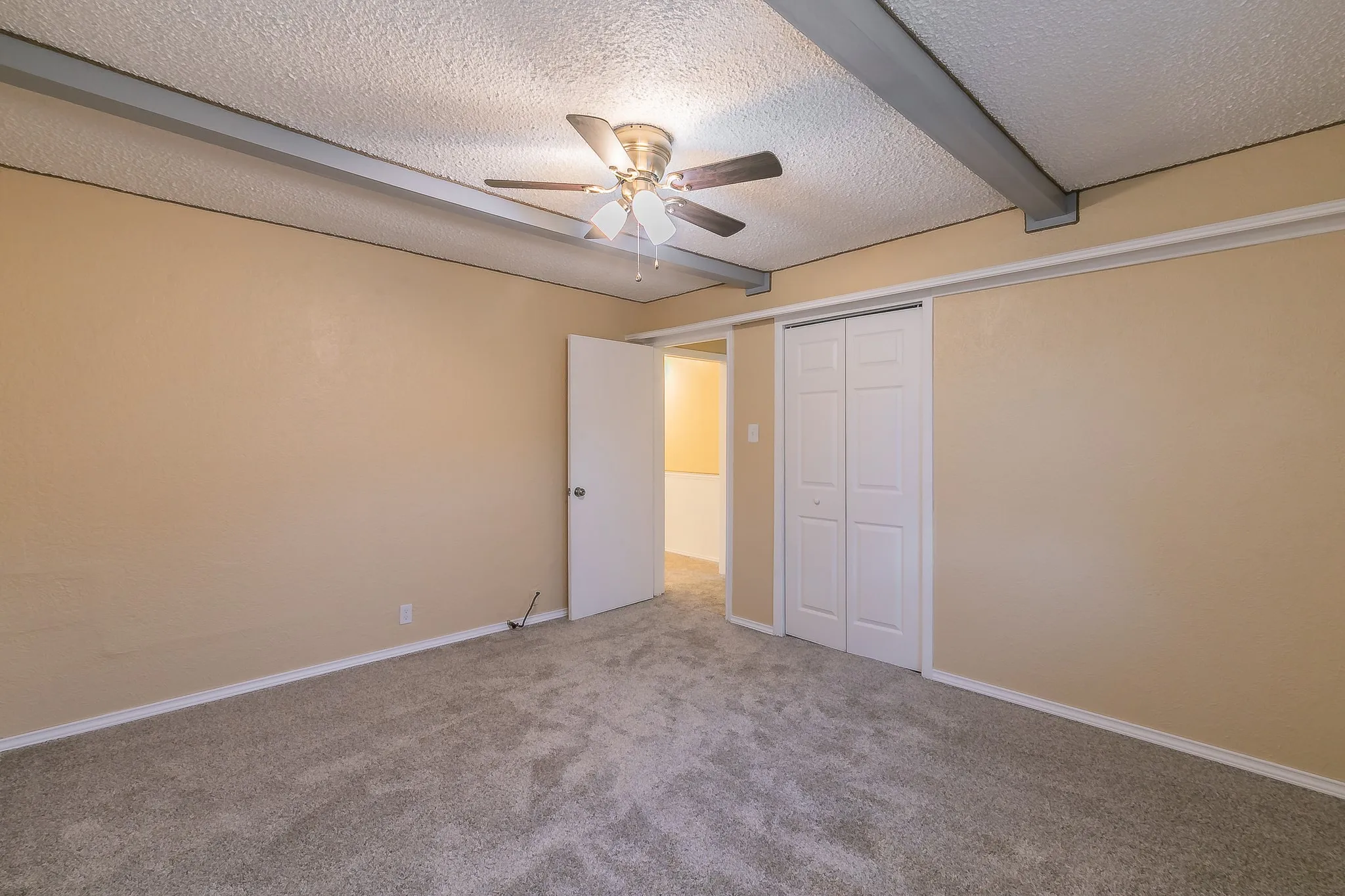 Unfurnished bedroom featuring ceiling fan, beamed ceiling, a textured ceiling, a closet, and carpet