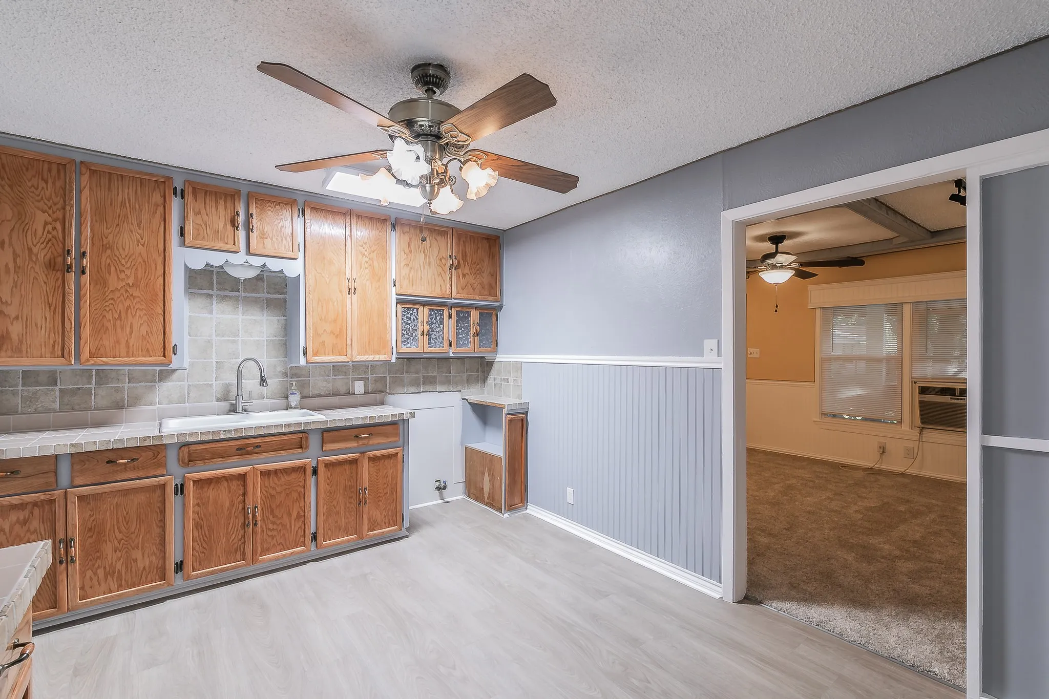 Kitchen featuring ceiling fan, sink, light hardwood / wood-style floors, a textured ceiling, and decorative backsplash