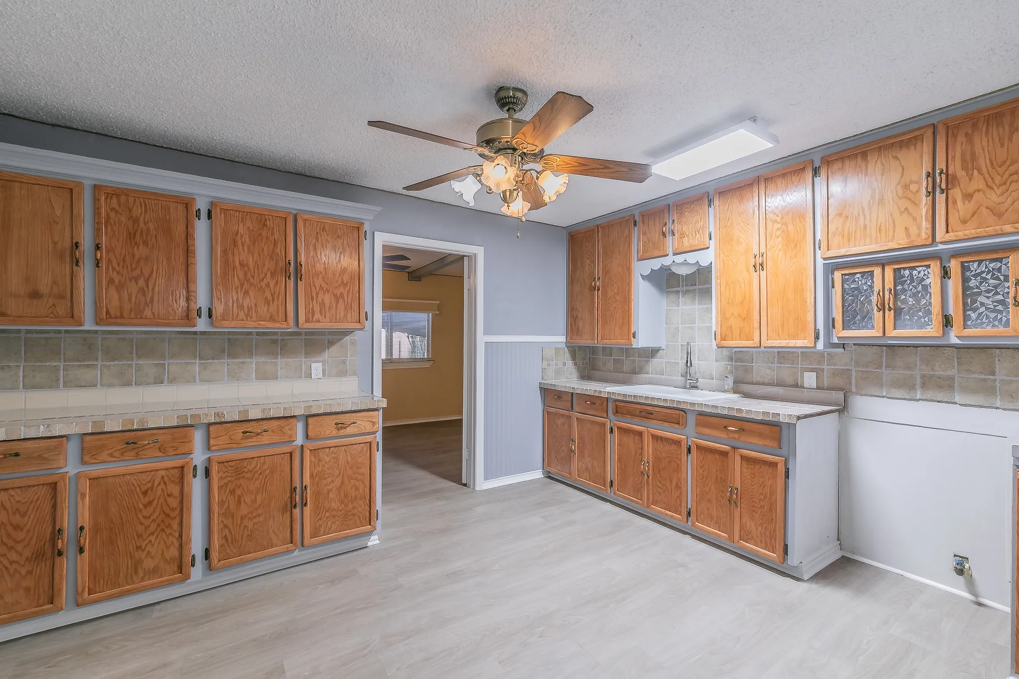 Kitchen with ceiling fan, light wood-type flooring, decorative backsplash, and sink
