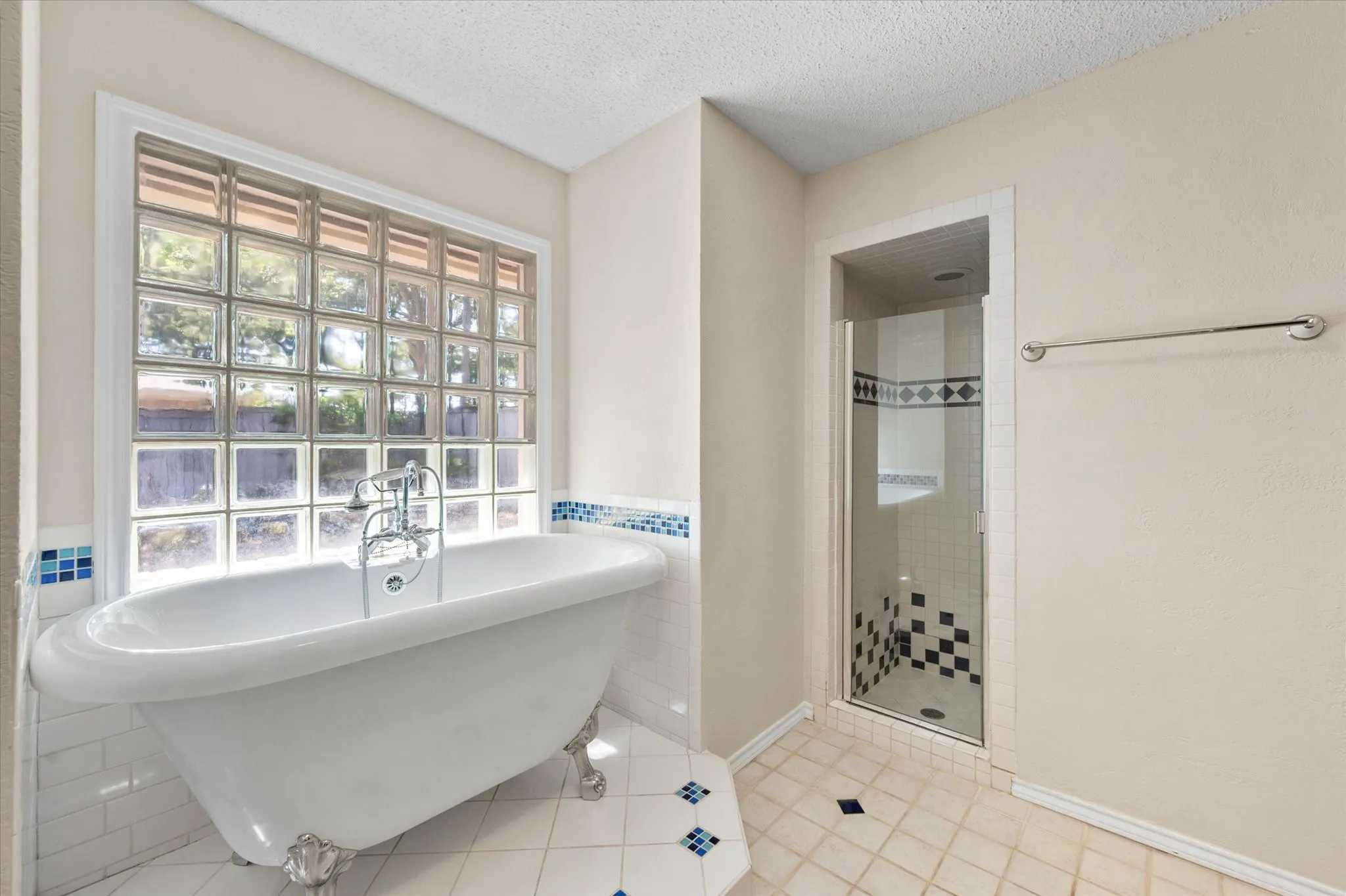 Freestanding clawfoot tub with polished chrome faucet, glass block window, separate shower enclosure with decorative tile accents, and tiled flooring