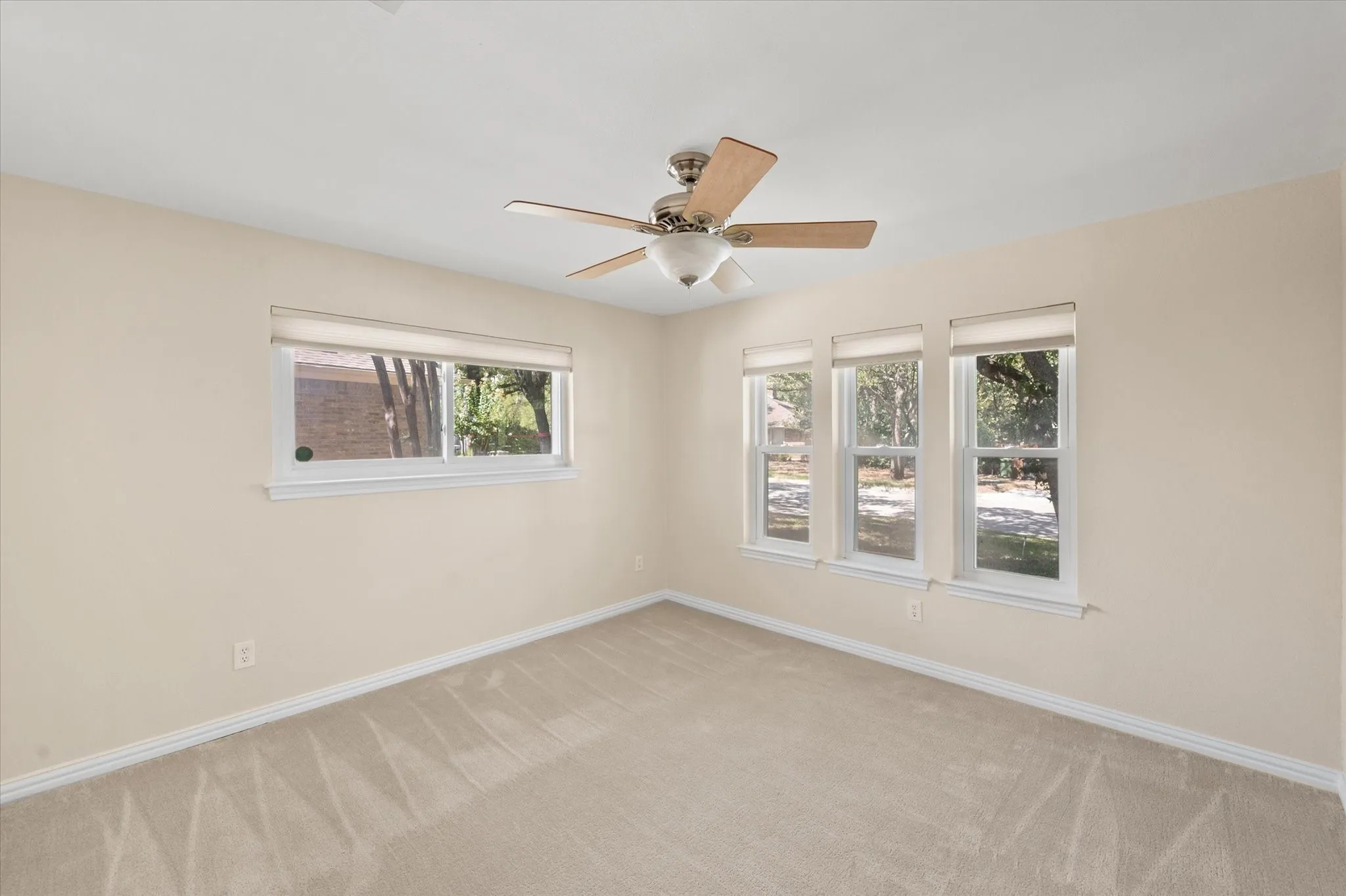 Neutral-toned carpeted flooring, multiple double-pane windows, and a ceiling-mounted light fixture with a five-blade fan
