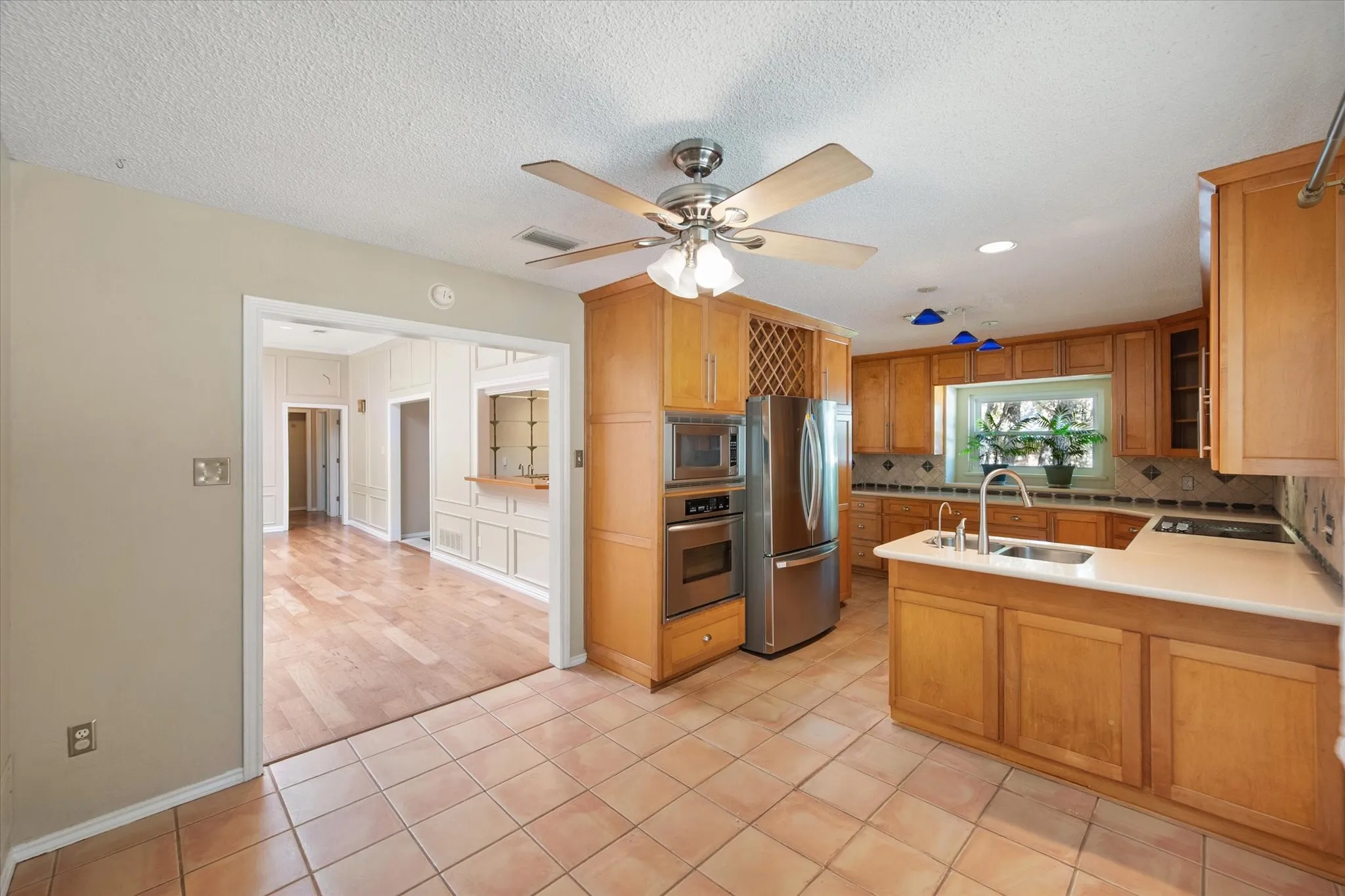 Kitchen featuring light wood cabinetry, stainless steel appliances, built-in wine storage, solid-surface countertops, and tile flooring